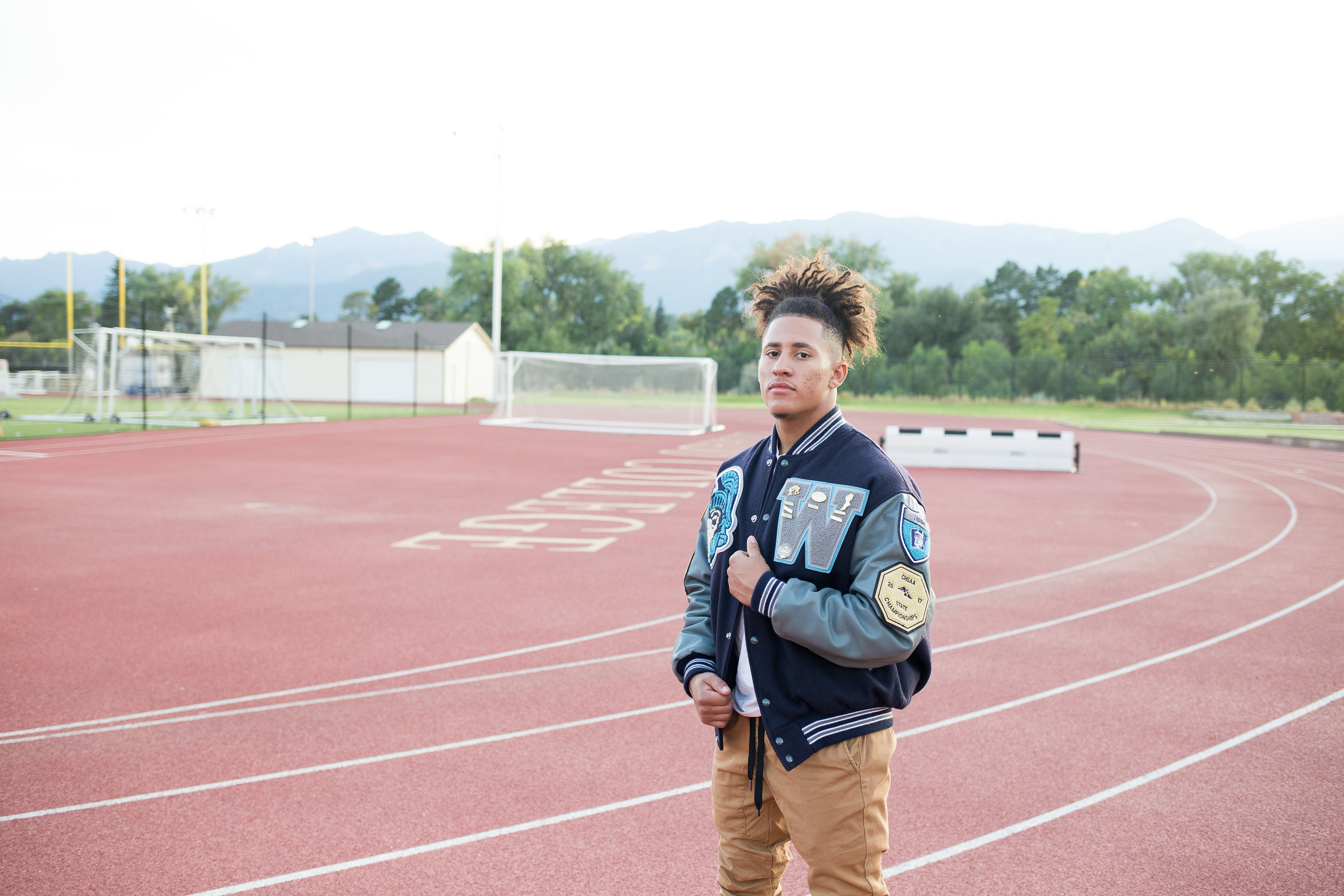 Senior standing on a track holding his varsity jacket while looking at the camera seriously Stacy Carosa Photography