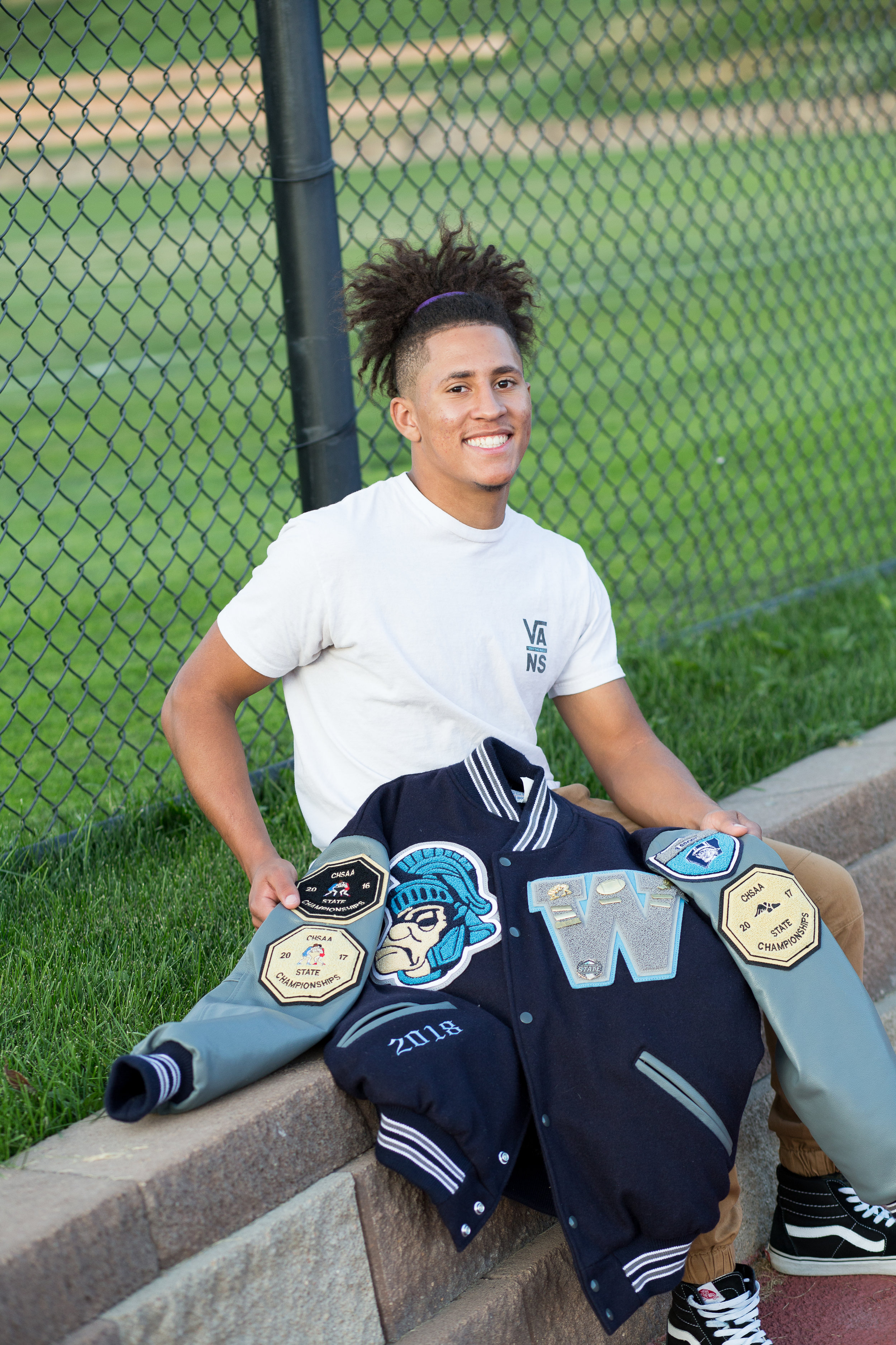 Widefield High  School senior sitting and holding his varsity jacket for his Colorado Spring senior photo session Stacy Carosa Photography