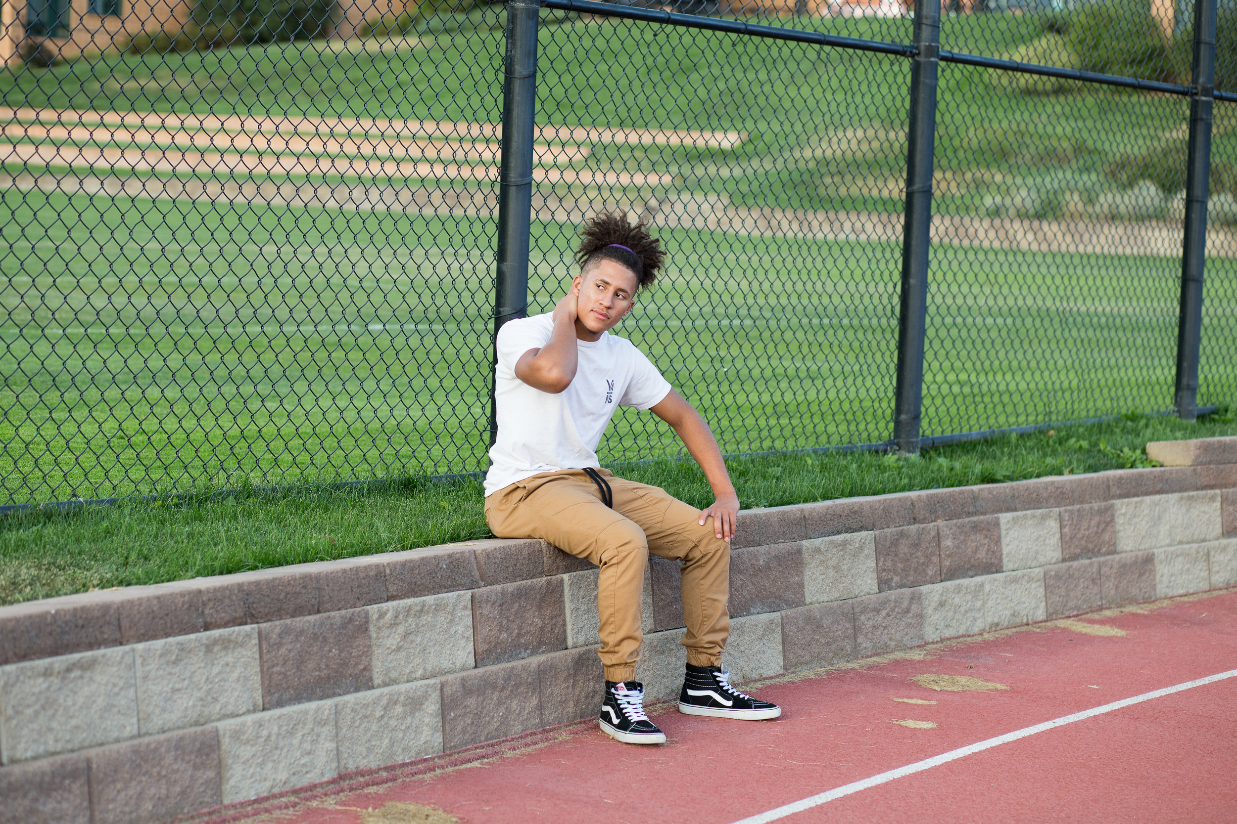 Boy sitting on a stone wall and rubbing neck next to a track in Colorado  Springs Stacy Carosa Photography