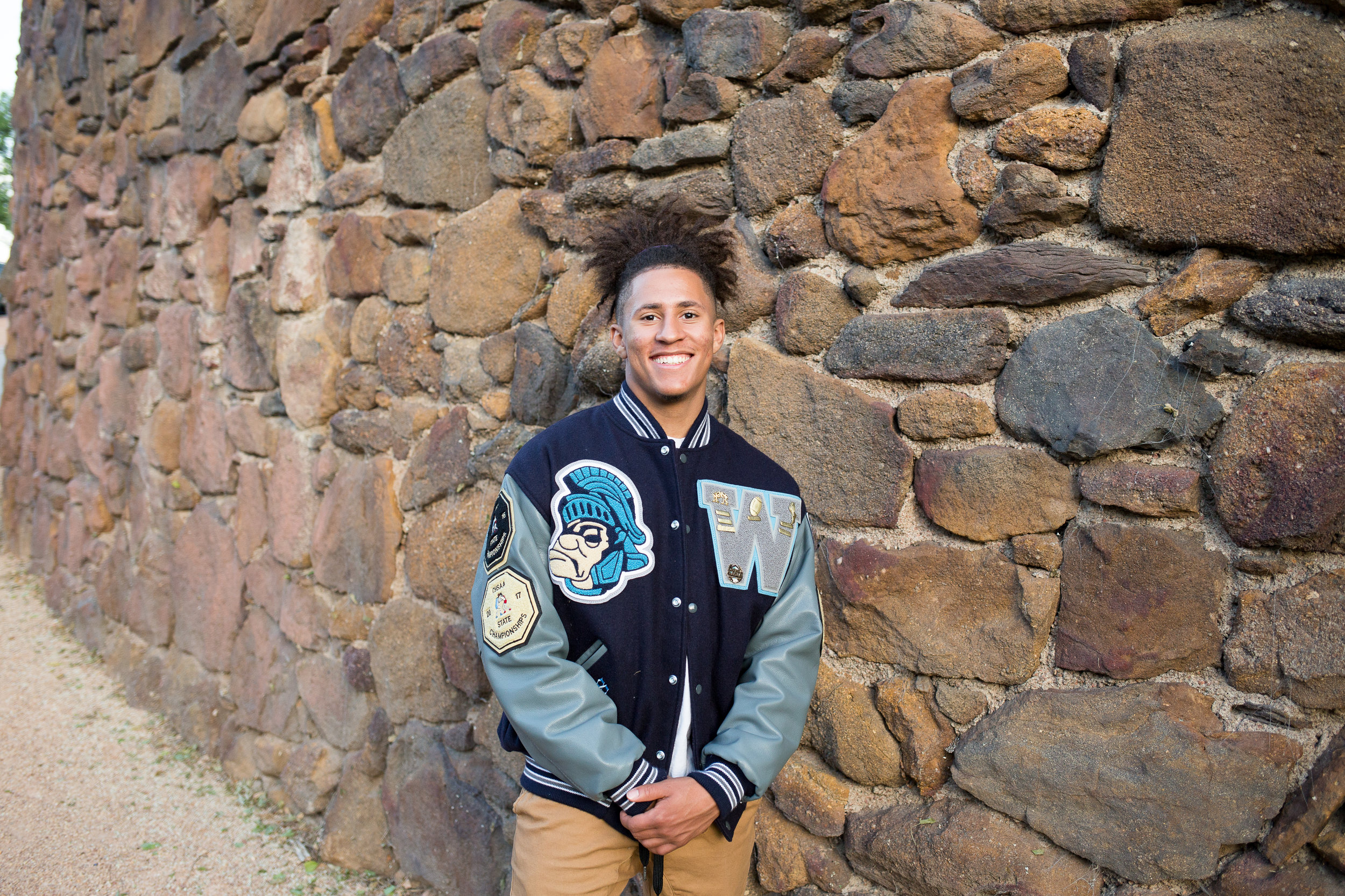 Colorado  Springs senior photo session downtown leaning against big stone wall in varsity jacket Stacy Carosa Photography