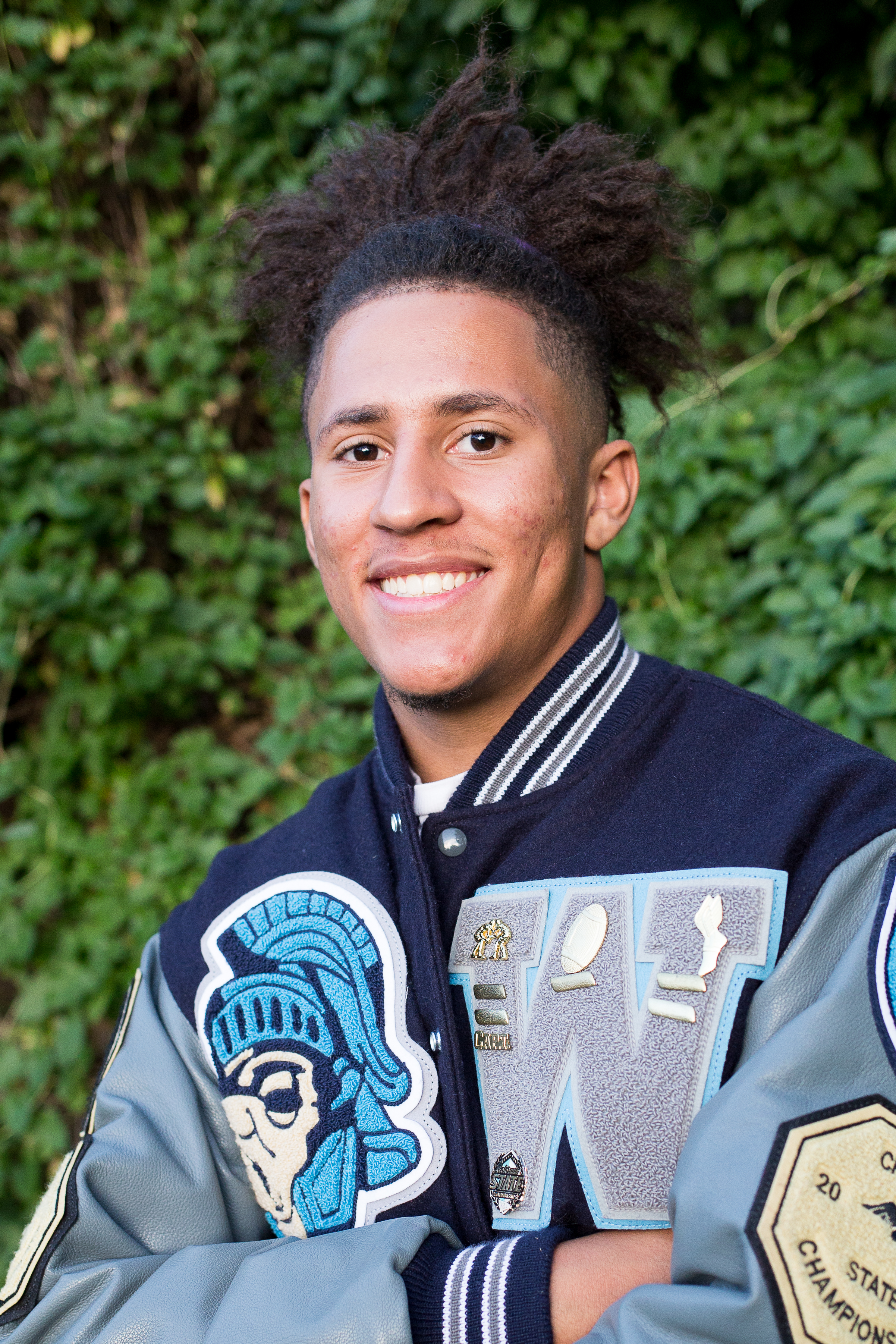 Head shot of a Widefield High School senior in  their varsity jacket in front of a green wall smiling Stacy Carosa Photgraphy Colorado Springs senior photos