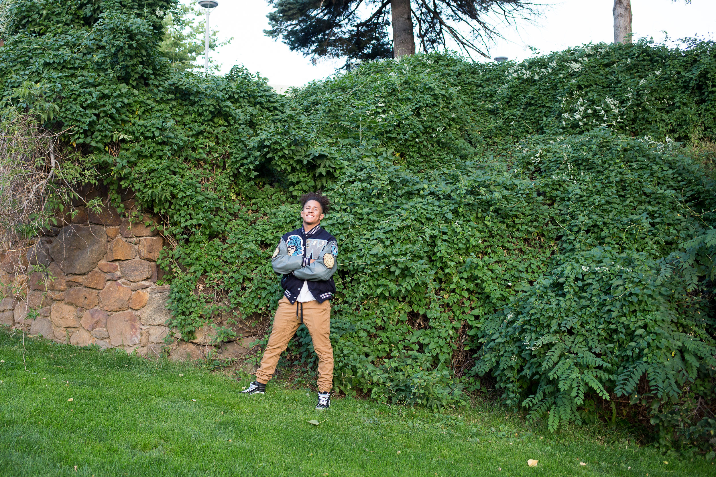 Widefield High School senior in varsity jacket standing in front of a wall of ivy for senior photos Stacy Carosa Photography Colorado Springs