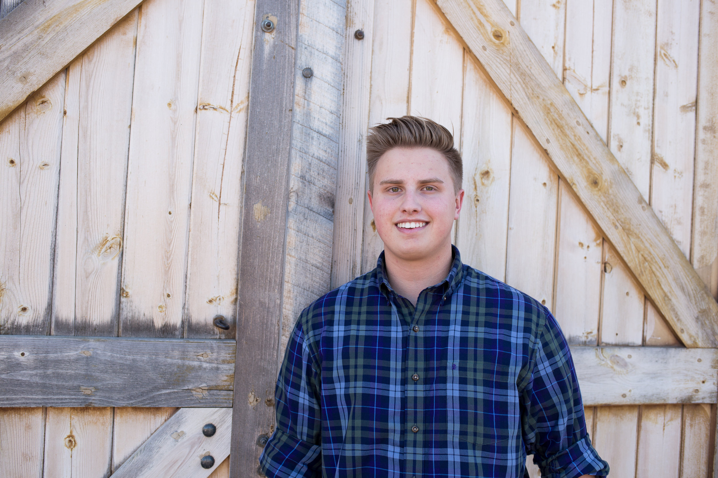 St. Mary's Senior Photos at Rock Ledge Ranch leaning against a barn door in a flannel shirt Stacy Carosa Photography Colorado Springs