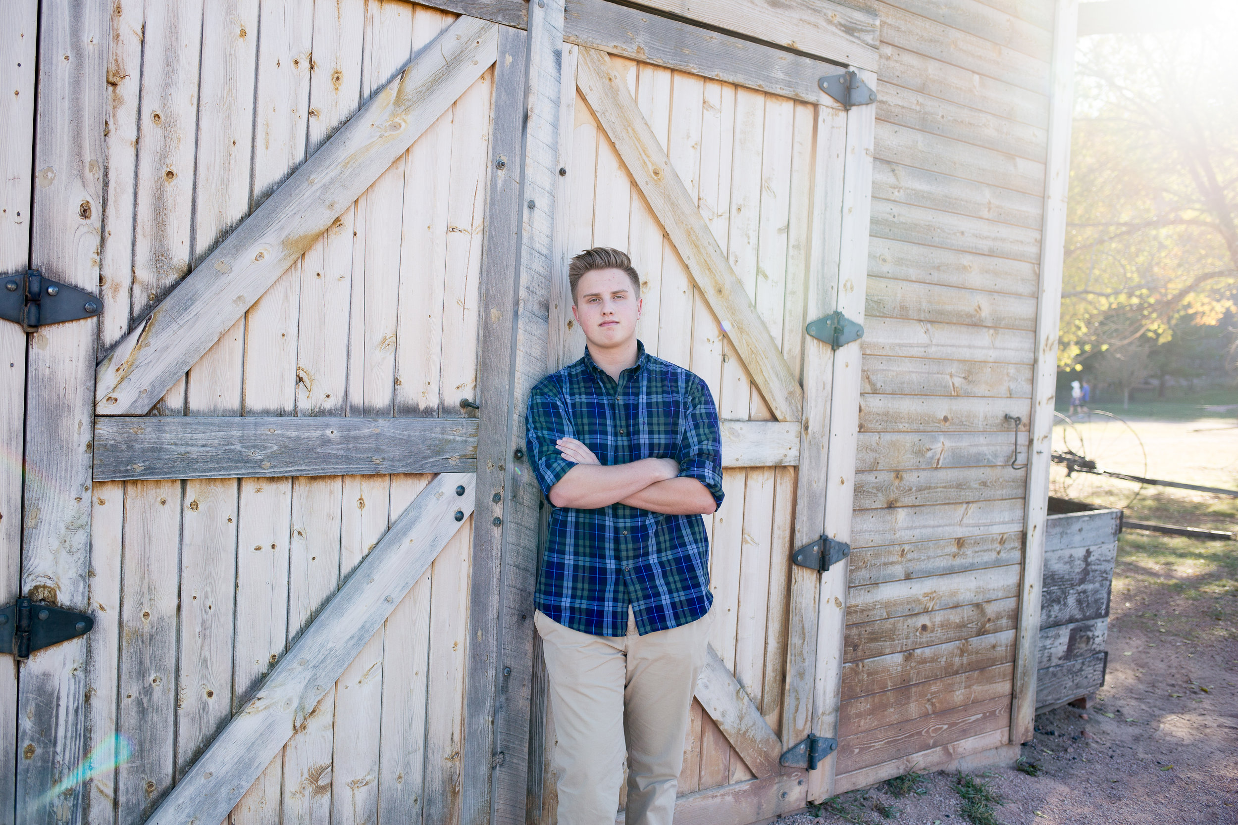 Senior boy leaning against barn door with arms crossed at Rock Ledge Ranch for senior photo session Stacy Carosa Photography Colorado Springs seniors