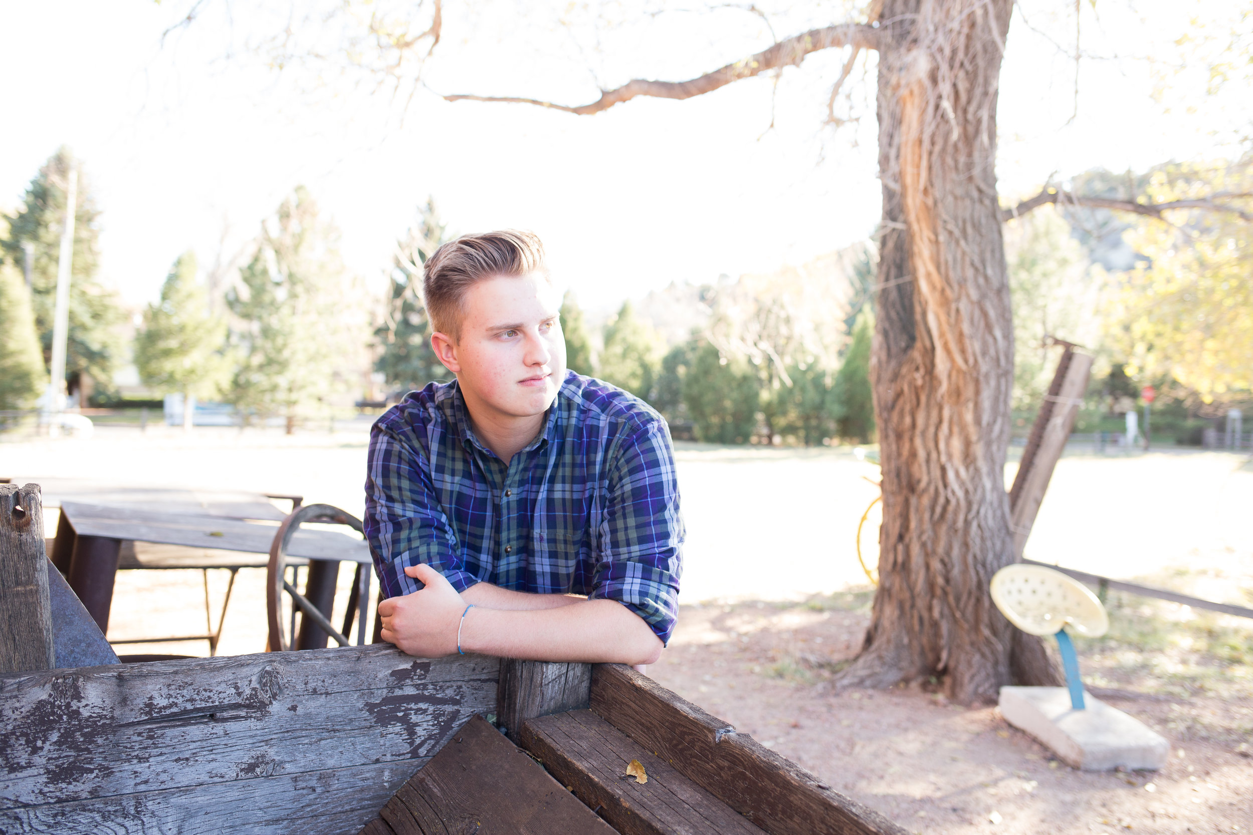 Senior leaning against crate at Rock Ledge Ranch with sunlight on his face and looking in distance Stacy Carosa Photography Colorado Springns Rock Ledge Ranch