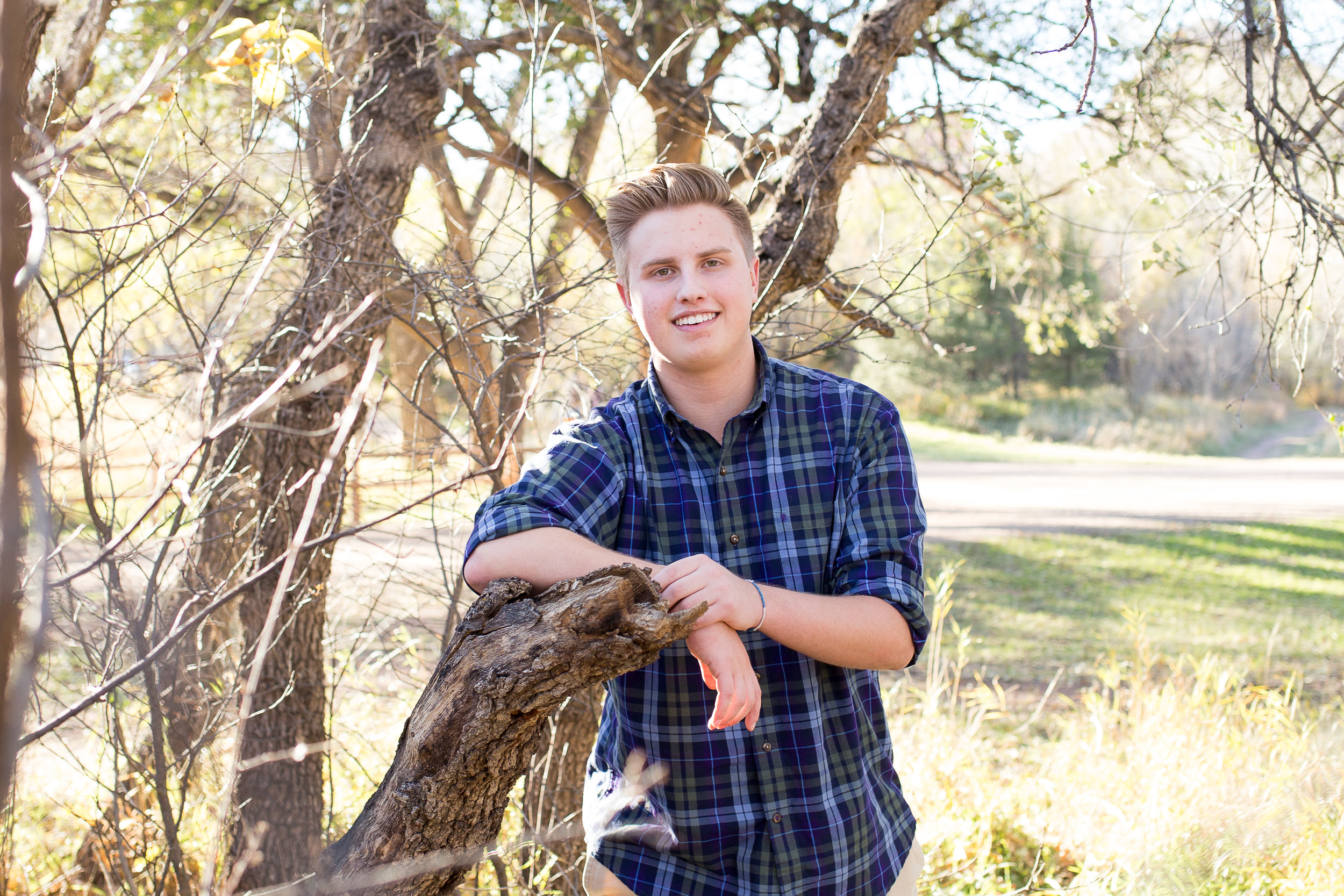 Senior boy with elbow leaning on a downed tree and smiling at the camera at Rock Ledge Ranch Colorado Springs senior session Stacy Carosa Photography