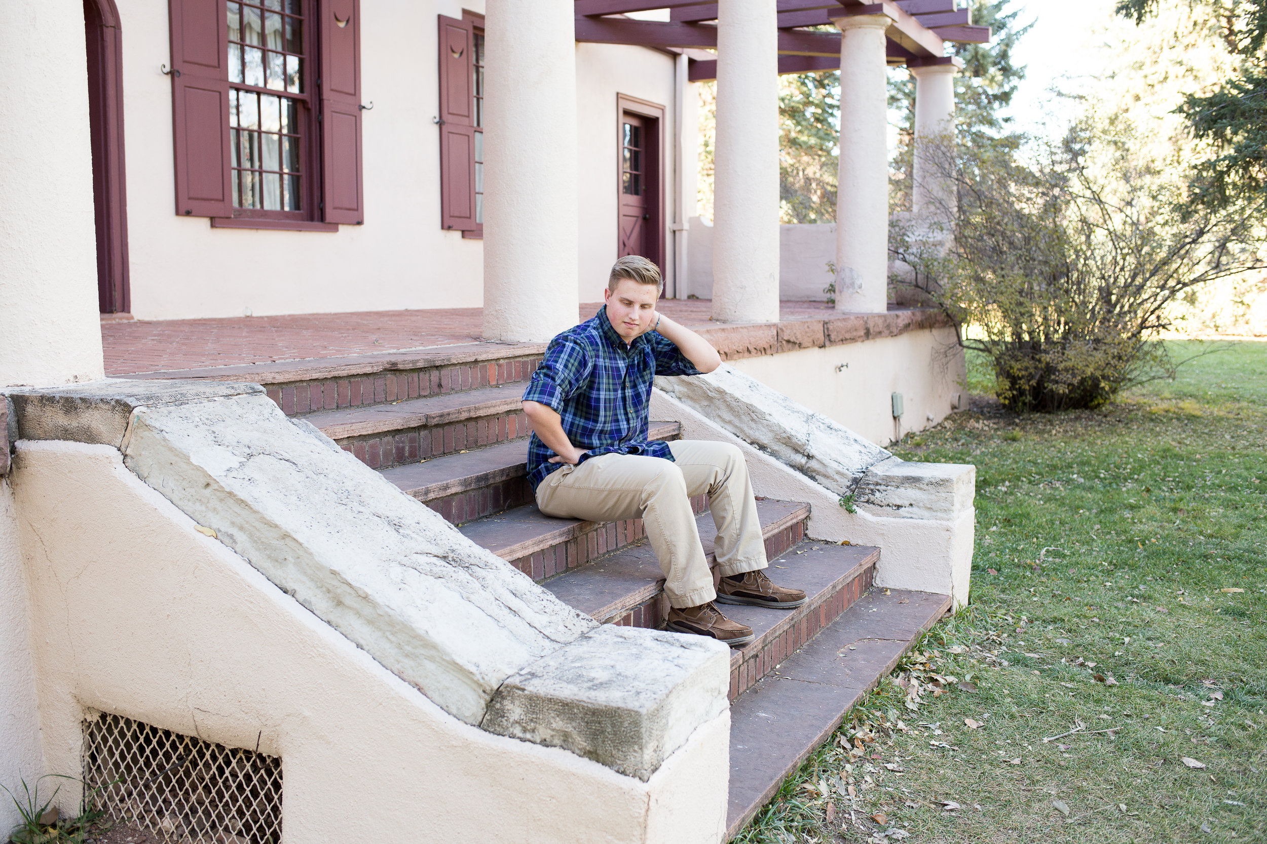 Colorado Springs senior photos at Rock Ledge Ranch senior sitting on stairs with hand on neck Stacy Carosa Photography