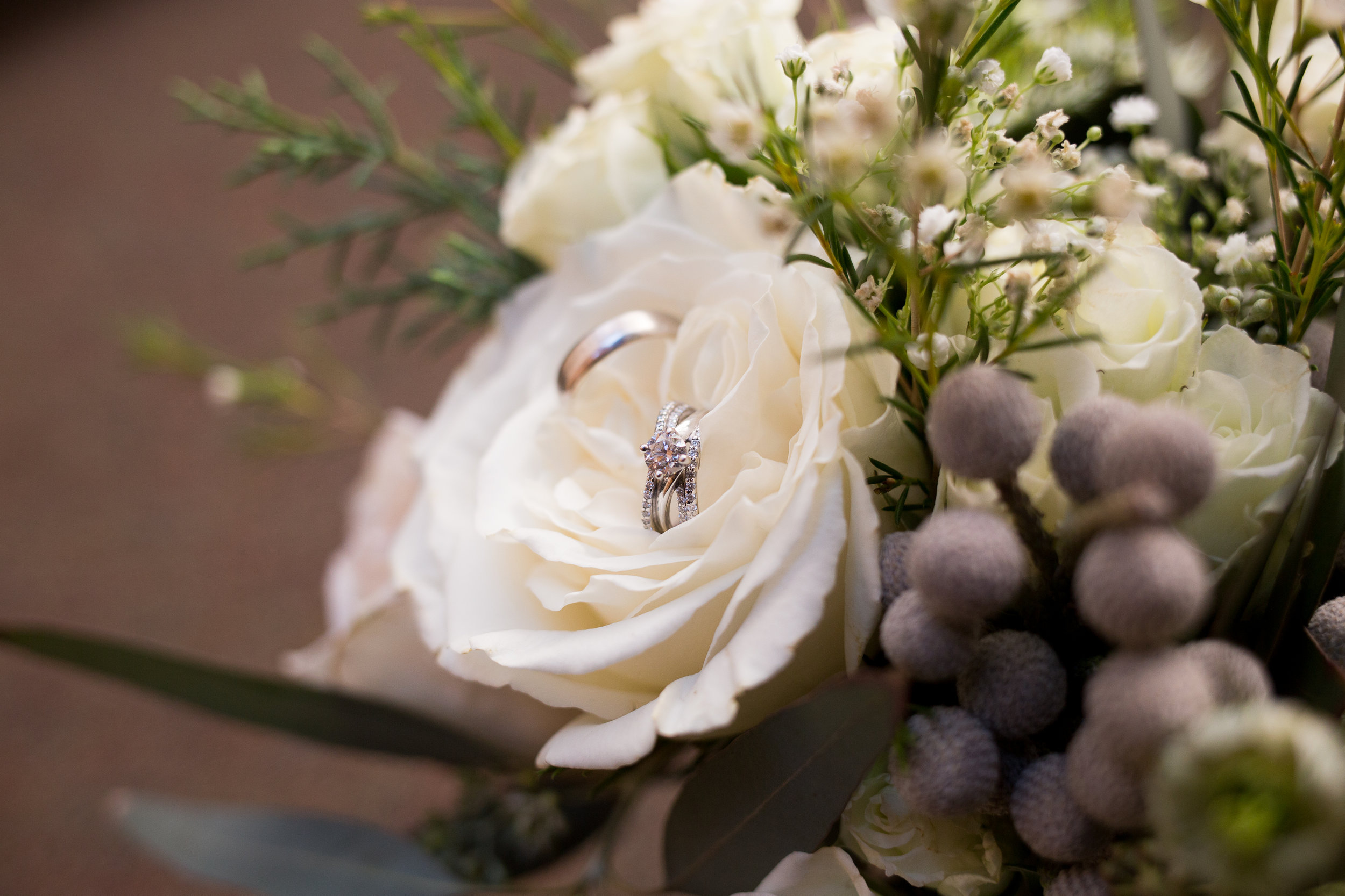 White flowers in a bridal bouquet with wedding rings sitting in a rose Stacy Carosa Photography Colorado Springs Winter Wedding
