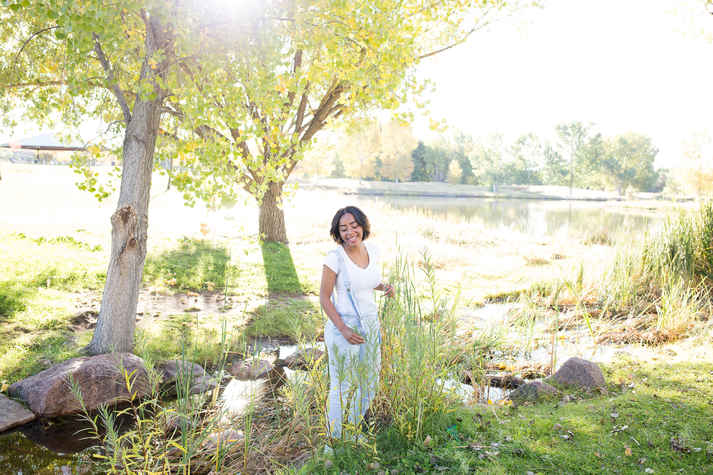 Beautiful morning light coming through tree and highlighting senior girl standing in the tall grasses at Fountain Creek Regional Park for senior photo Stacy Carosa Photography