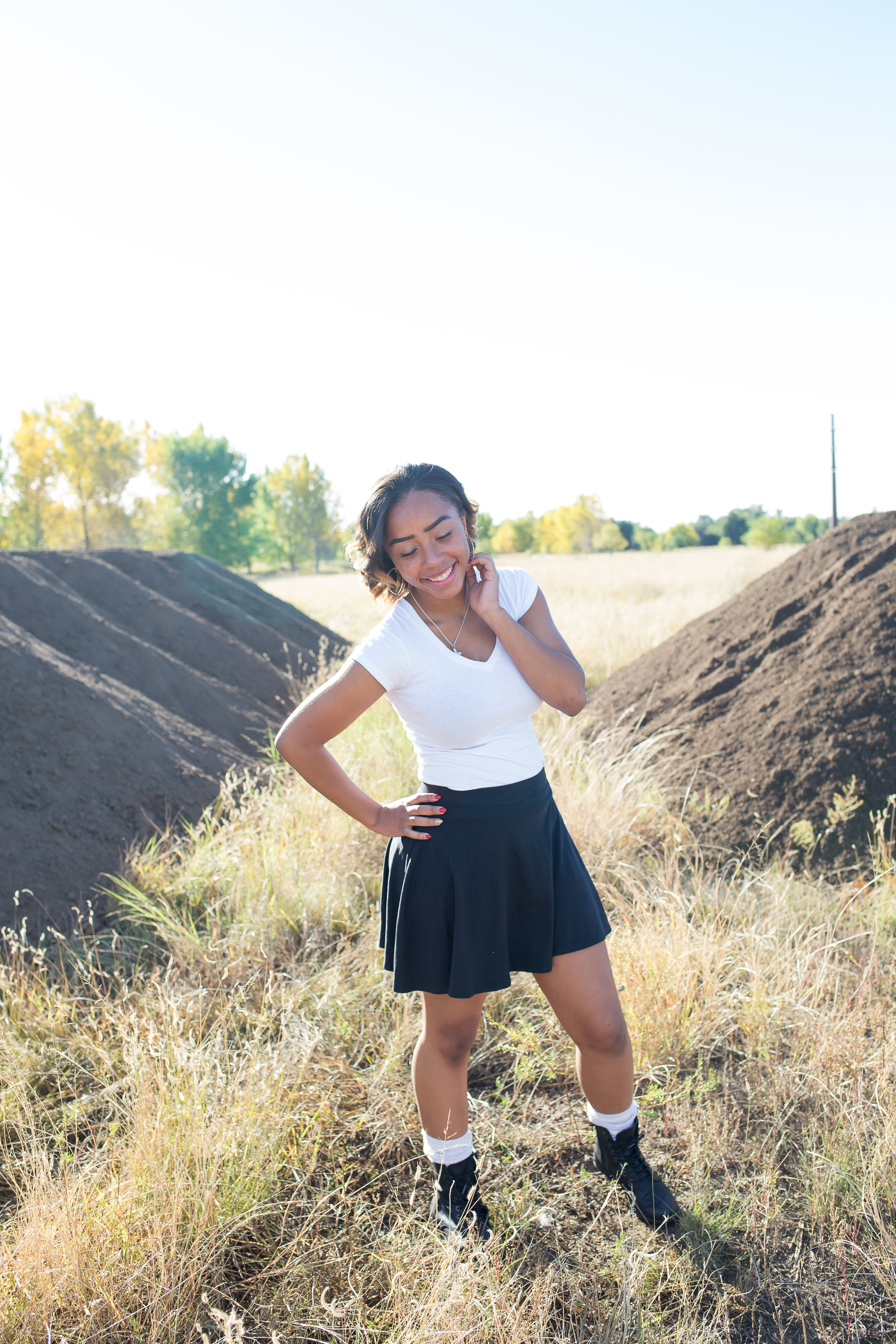 Widefield High School senior girl standing with hand on hip looking at the ground laughing for senior photos at Fountain Creek Regional Park in Colorado Springs, CO Stacy Carosa Photography