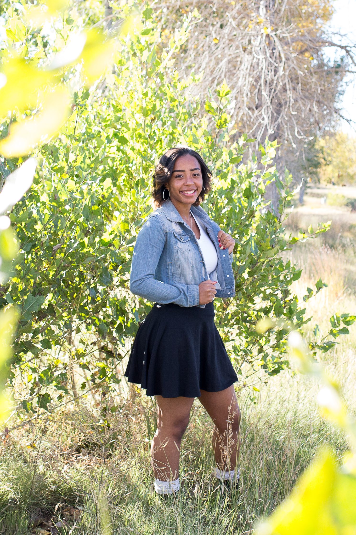 Girl standing among the green trees holding her jean jacket for her senior portraits in Fountain Creek  Regional Park Stacy Carosa Photography Colorado Springs Senior Photos