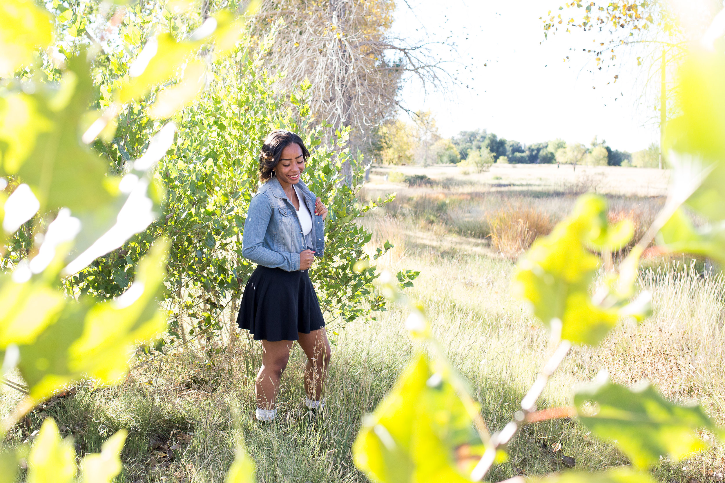 Girl standing by green trees with leaves in the foreground at Fountain Creek Regional Park Widefield High School Senior Stacy Carosa Photography