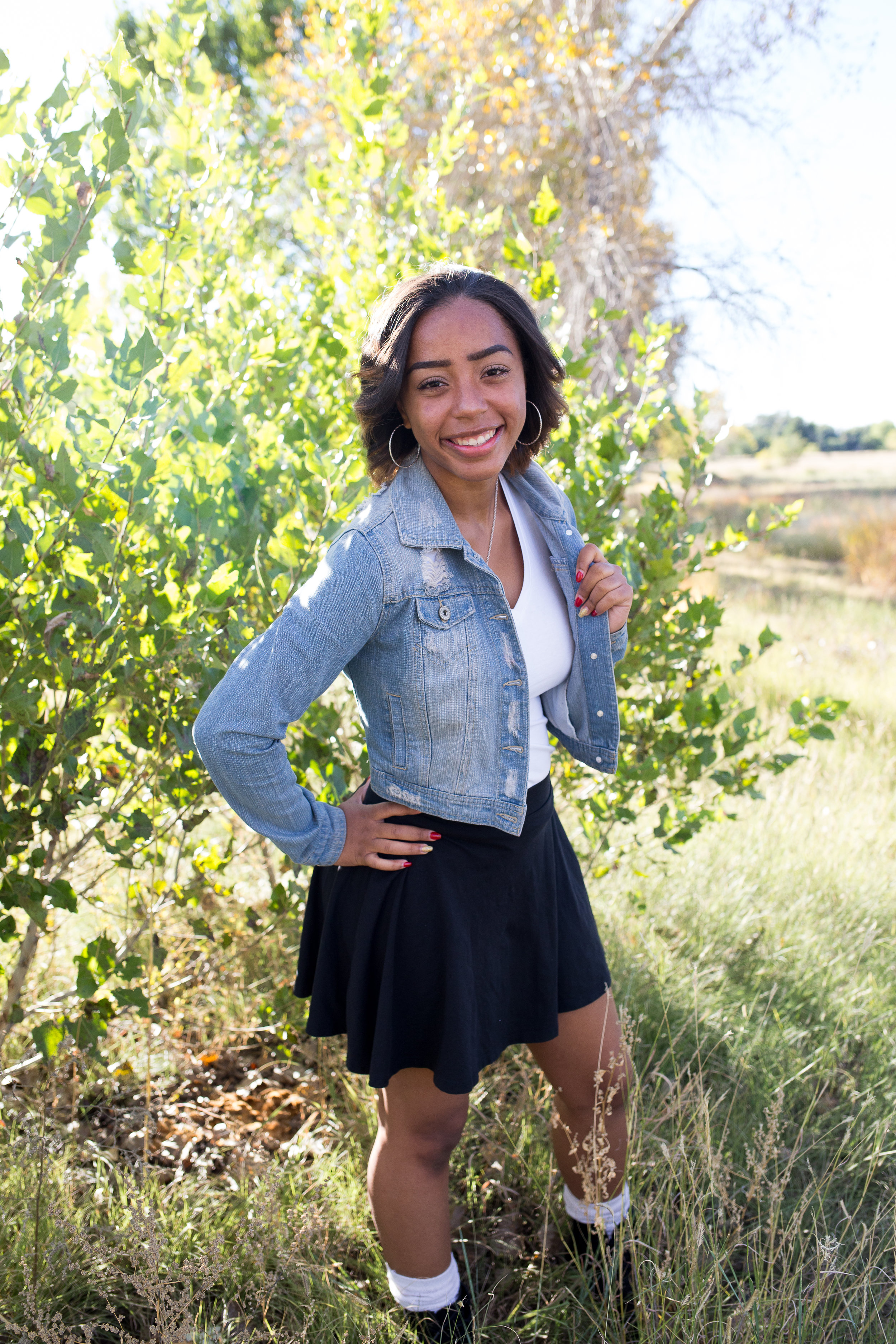 Girl in jean jacket standing among the green trees at Fountain Creek Regional Park in Colorado Springs, CO for senior photos Stacy Carosa Photography