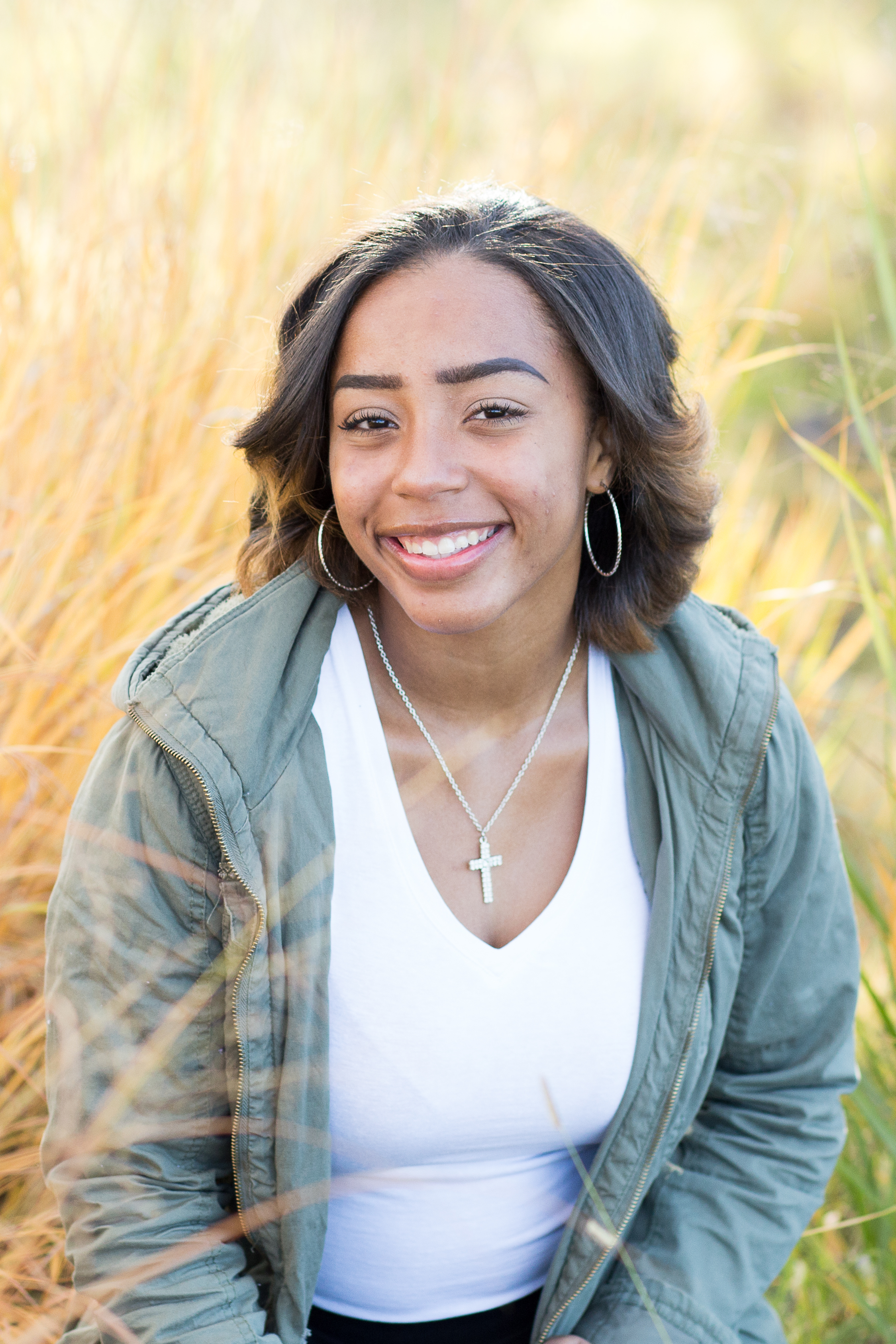 Girl sitting among the tall grasses with morning light hitting them at Fountain Creek Regional Park Widefield High School Senior Photos Stacy Carosa Photography