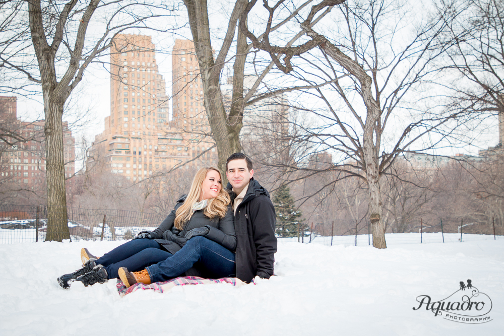 Engaged Couple smiling sitting in the snow in Central Park