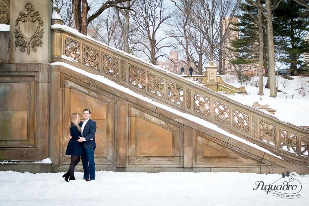 engaged couple embrace by snowy Bethesda Terrace