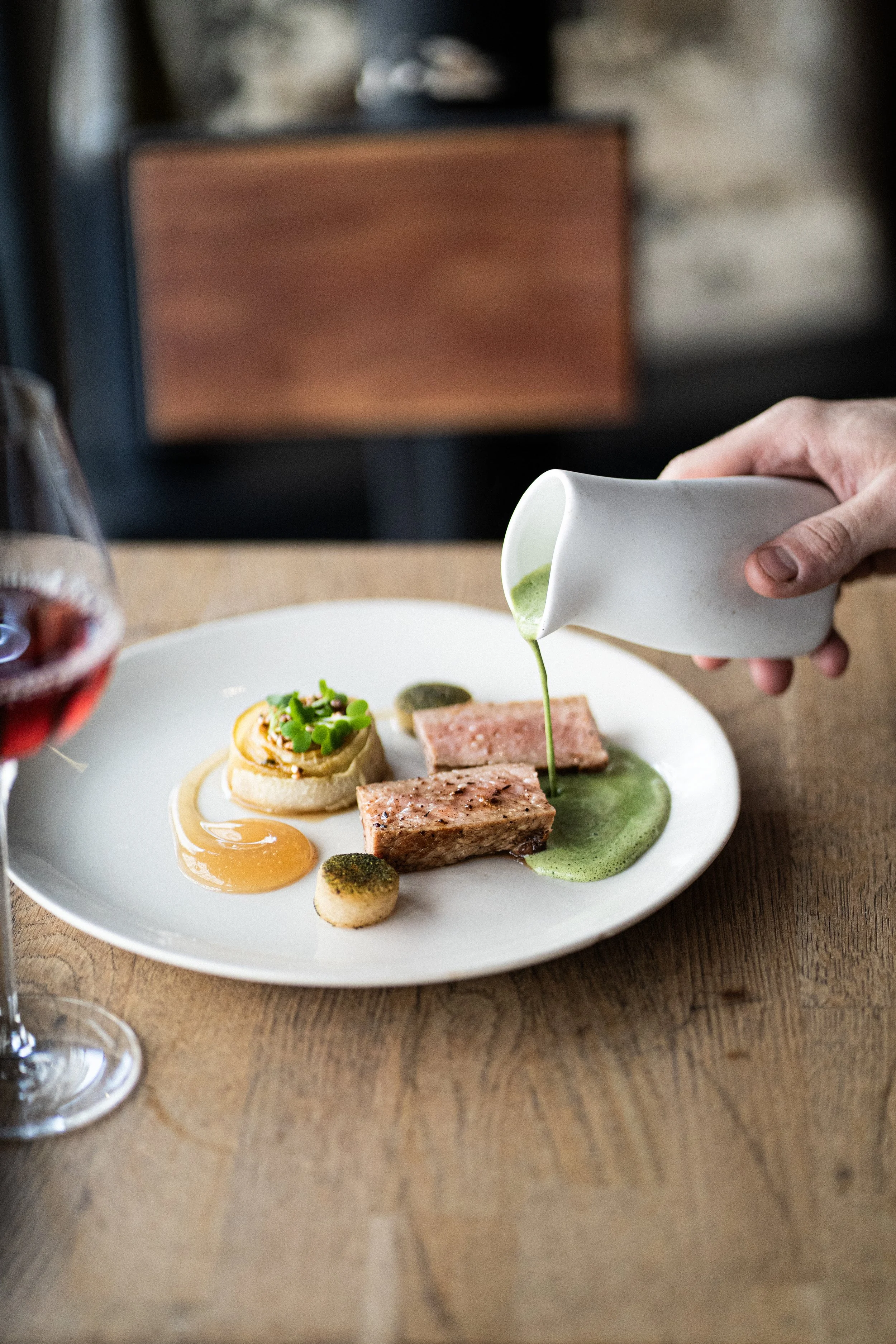 Assiette de plats gastronomiques avec des morceaux de viande, une mousse verte, une sauce orange, et une garniture décorative, service dans un restaurant