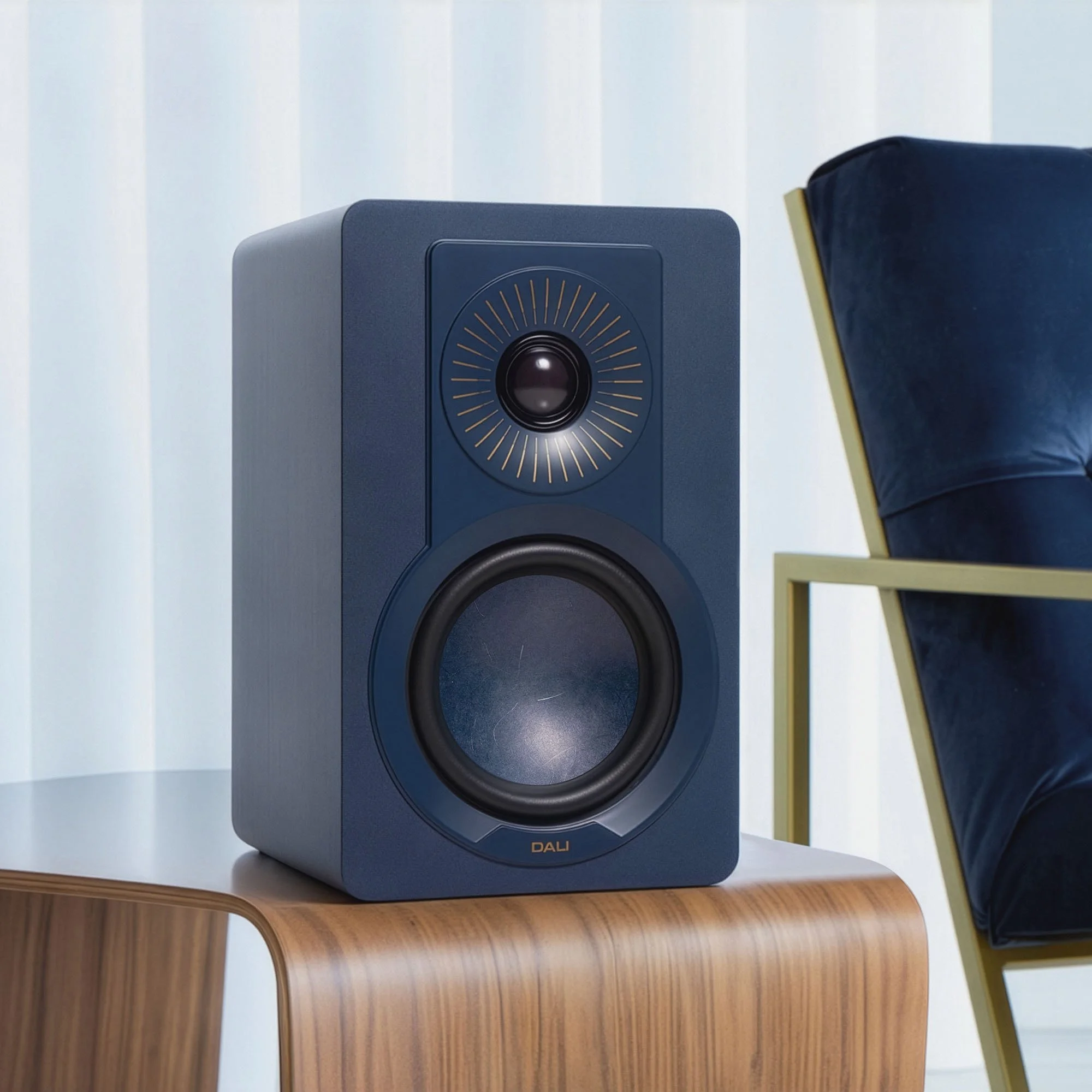 A chilly blue DALI Kupid bookshelf speaker pictured on a walnut side table.