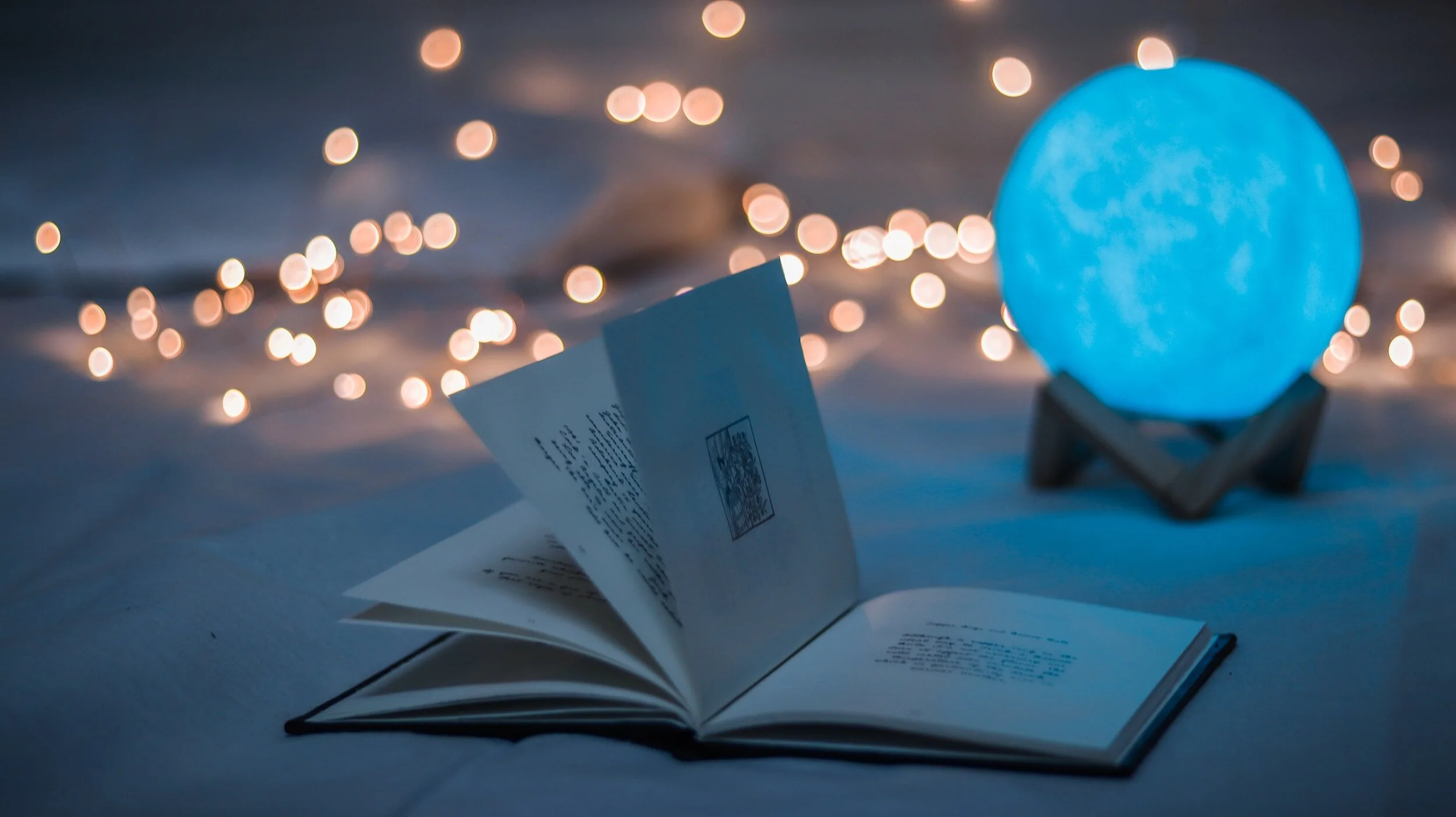 open book in front of a glowing blue moon like crystal ball with twinkle lights in the background