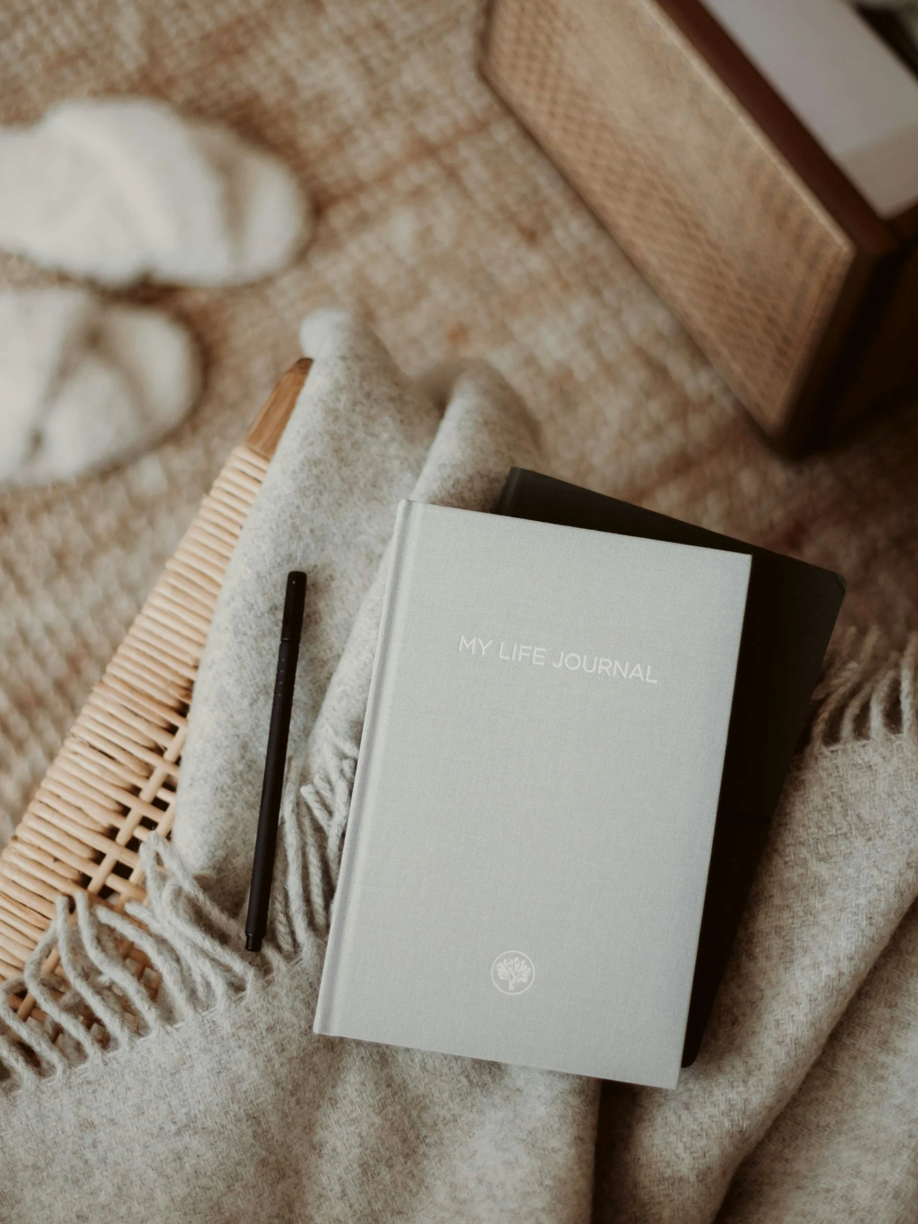 a white hardcover book that says 'my life journal' on a wicker chair covered with a cozy scarf