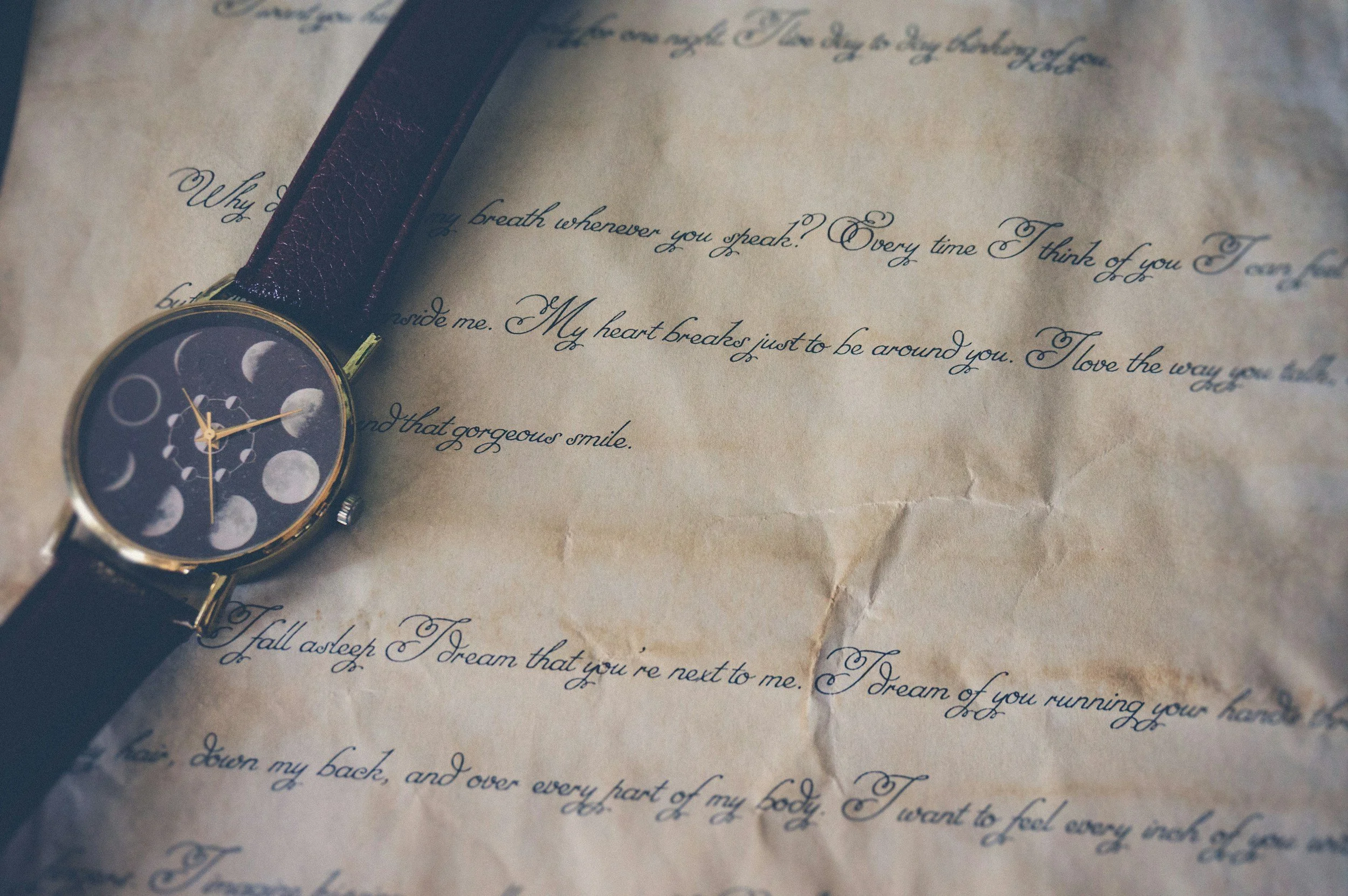 a black strapped watch with the face of being the moon phases sitting on cream colored paper with script writing