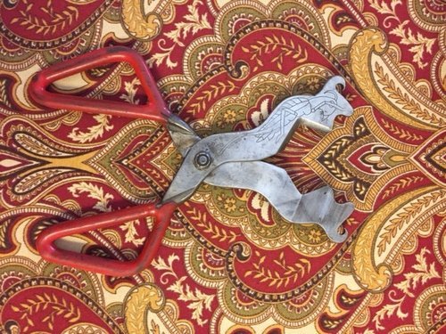 decorative pair of glassblowing shears laying on red and gold paisley fabric.JPG