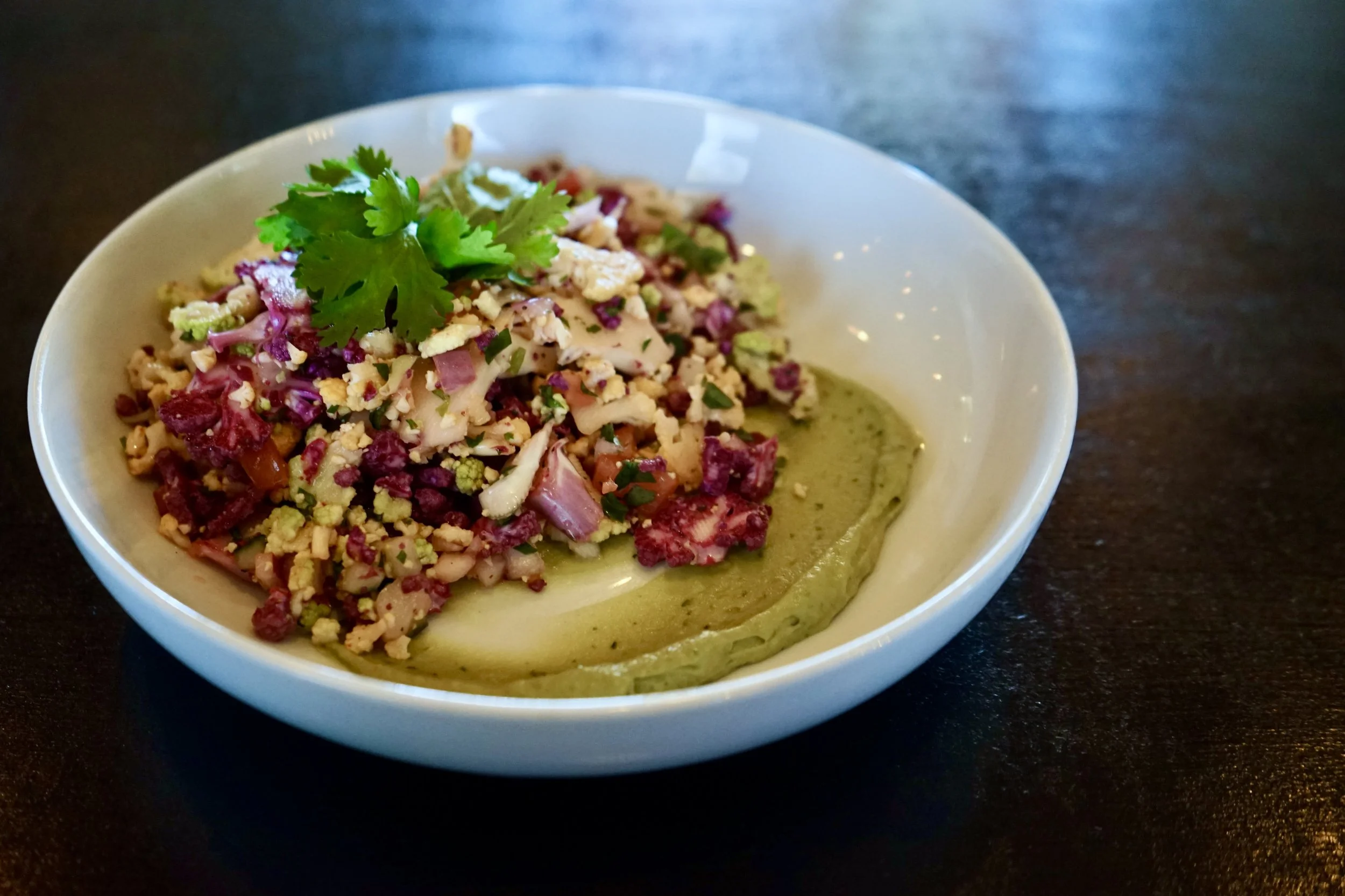 A bowl of mixed vegetable salad with cauliflower, red onion, and herbs, topped with cilantro, served on a green sauce.