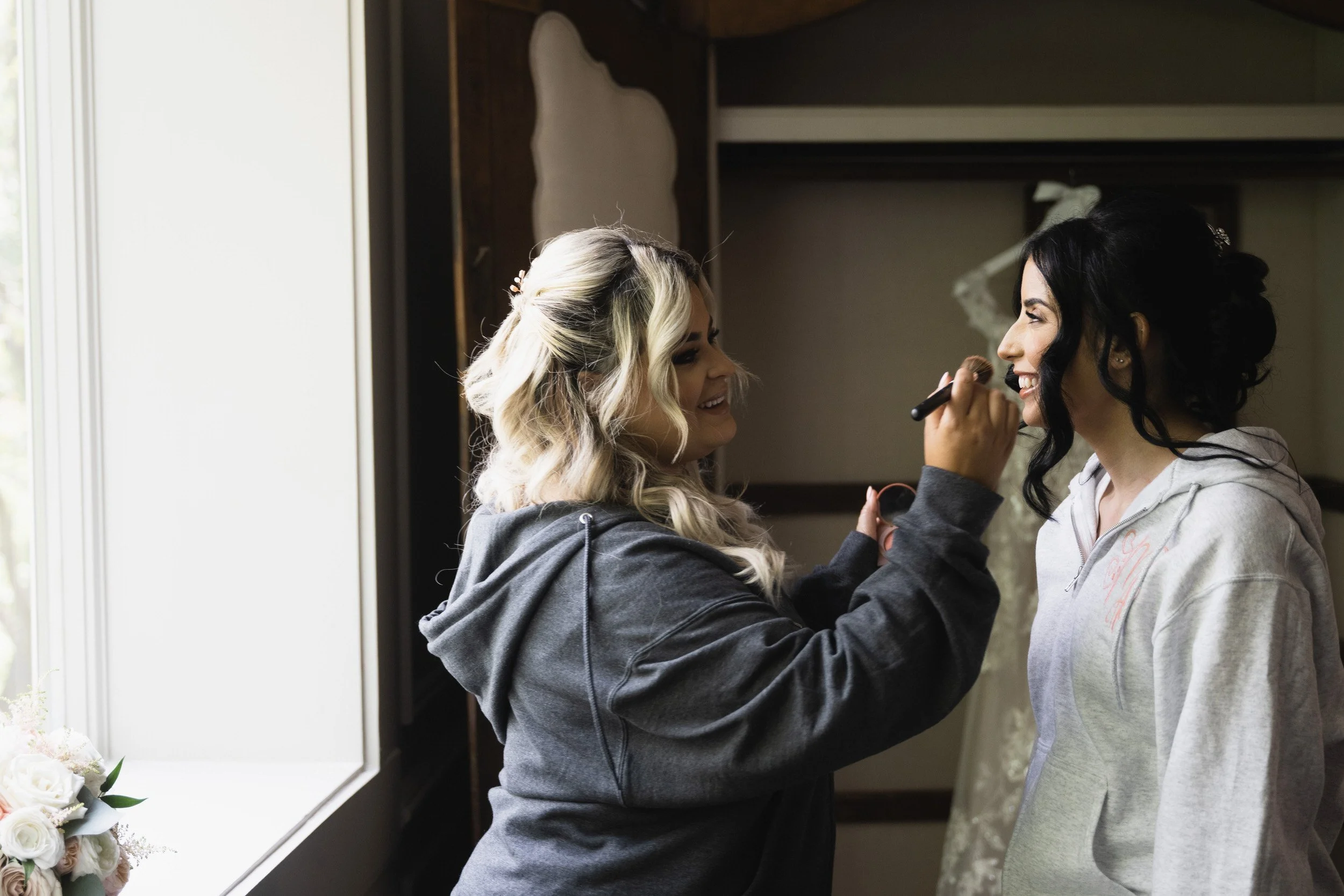 Bride getting makeup done by artist near window before Valley Regency wedding