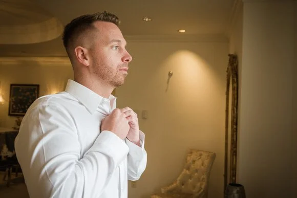 Groom adjusting his collar in the ballroom suite before the ceremony