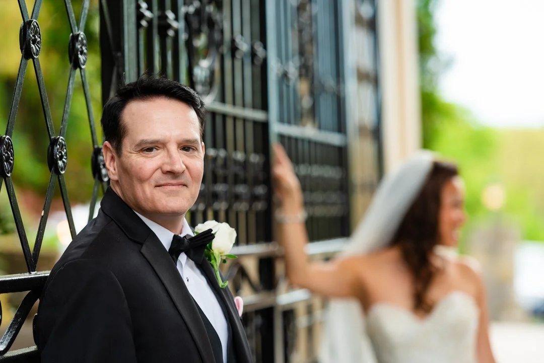 Groom portrait by the gates at Westmount Country Club with the bride softly blurred in the background.