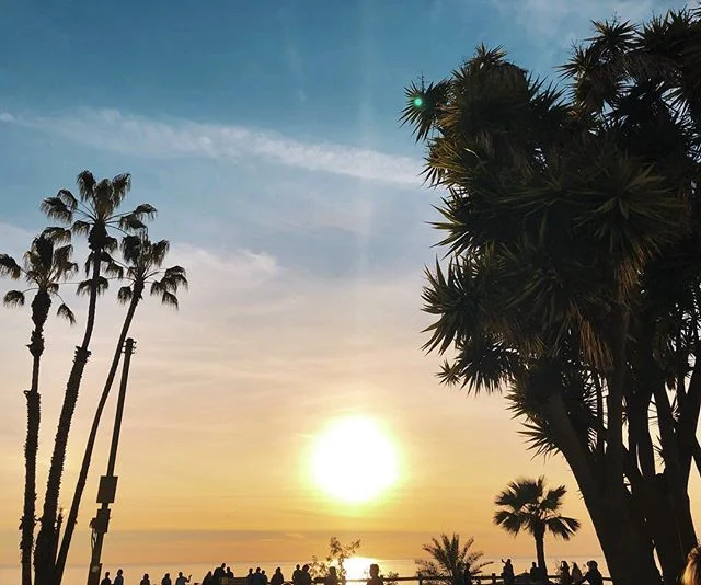 i&rsquo;m sitting alone on the grass, my back against a palm tree, overlooking the beach under the warm, golden light of the slowly setting sun. there&rsquo;s a wonderfully talented street performer nearby strumming his acoustic guitar, soulfully sin