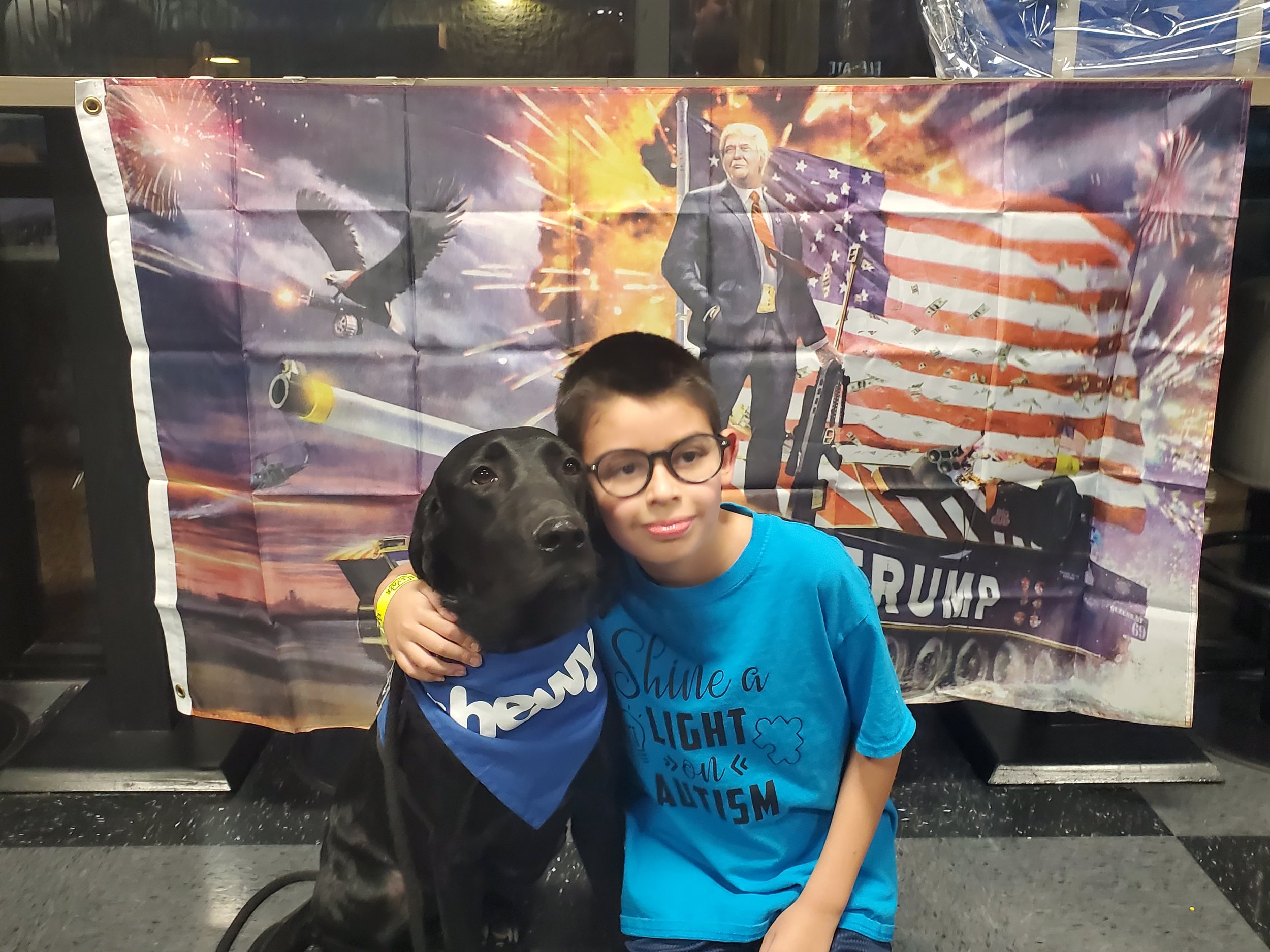 Boy in blue shirt embracing his black Labrador psychiatric service dog