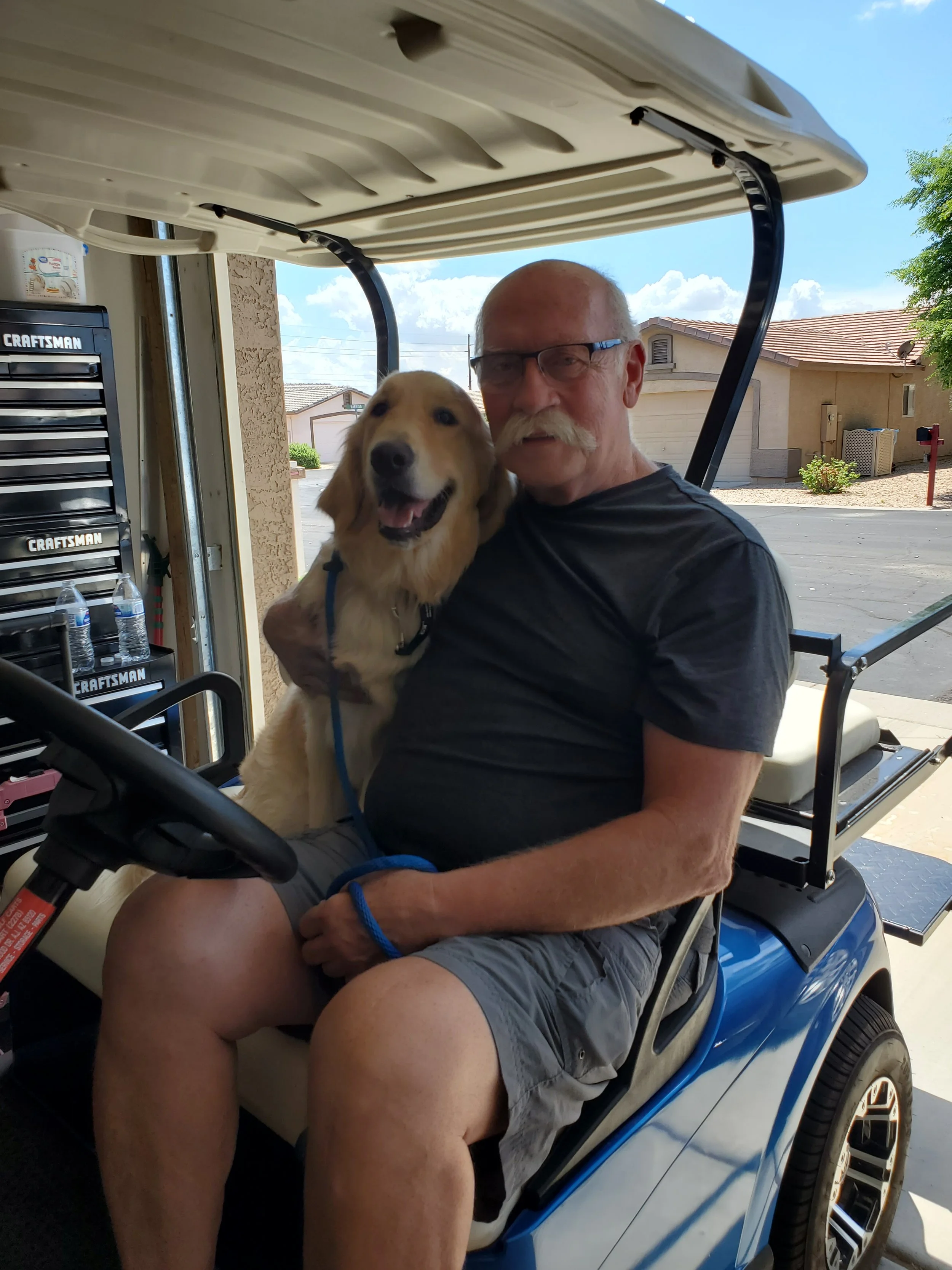 Man riding in a golf cart with his golden psychiatric service dog beside him.