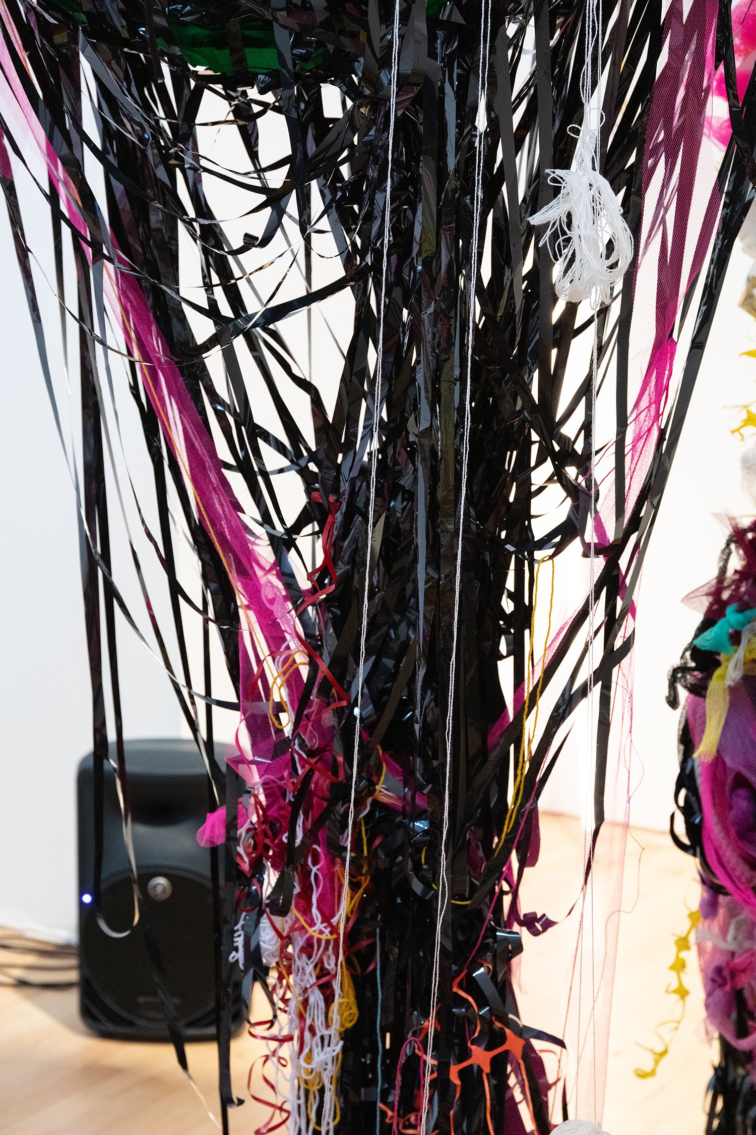 Detailed close-up of black tape strands hanging downward, interwoven with threads and small fragments of coloured material.