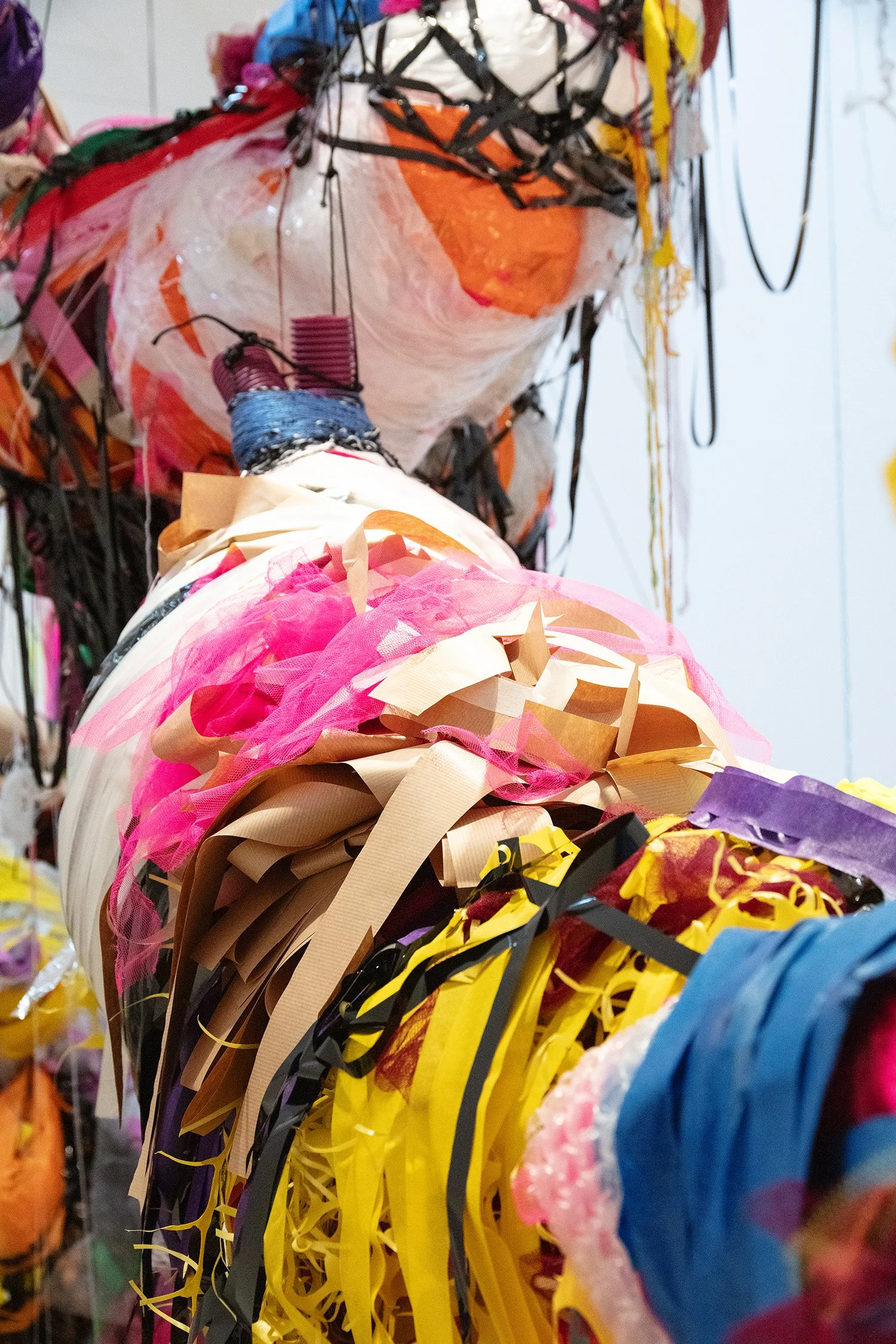 Close-up view between two sculptural forms, showing overlapping textures of plastic, fabric, and tape, with audio equipment visible on the floor in the background.