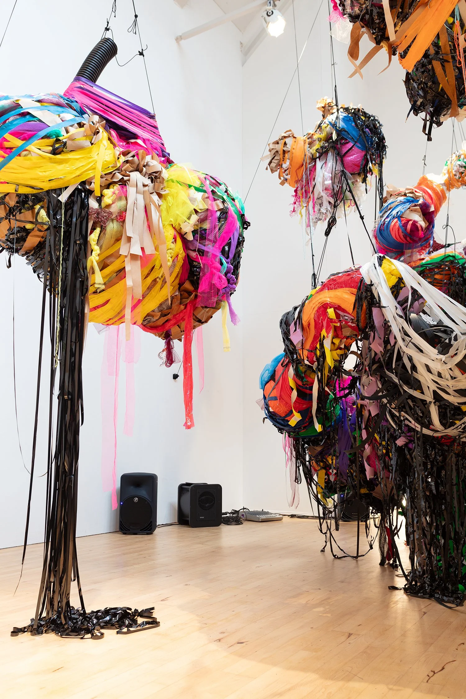 Mid-range view of clustered hanging sculptures, showing variation in scale and density, with materials gathered into rounded, organic shapes.