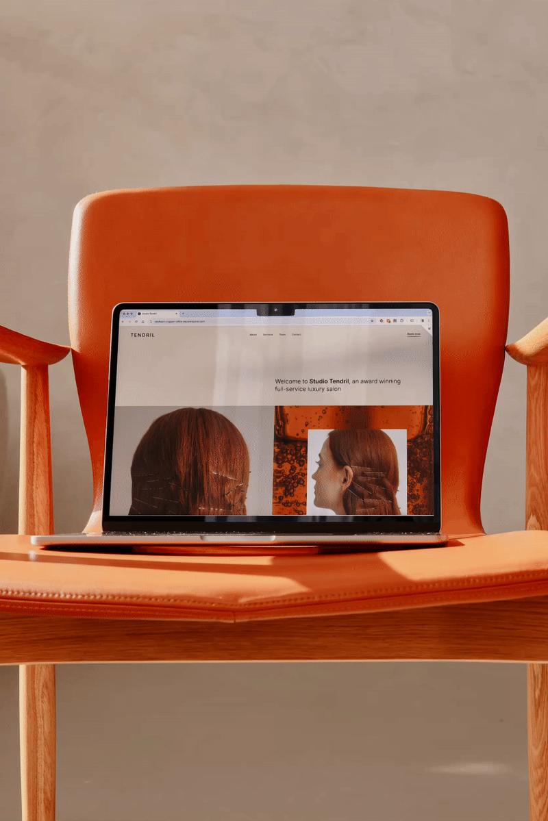 Laptop on an orange chair displaying the website of Studio Tendril, a luxury salon, with images of a woman with red hair.