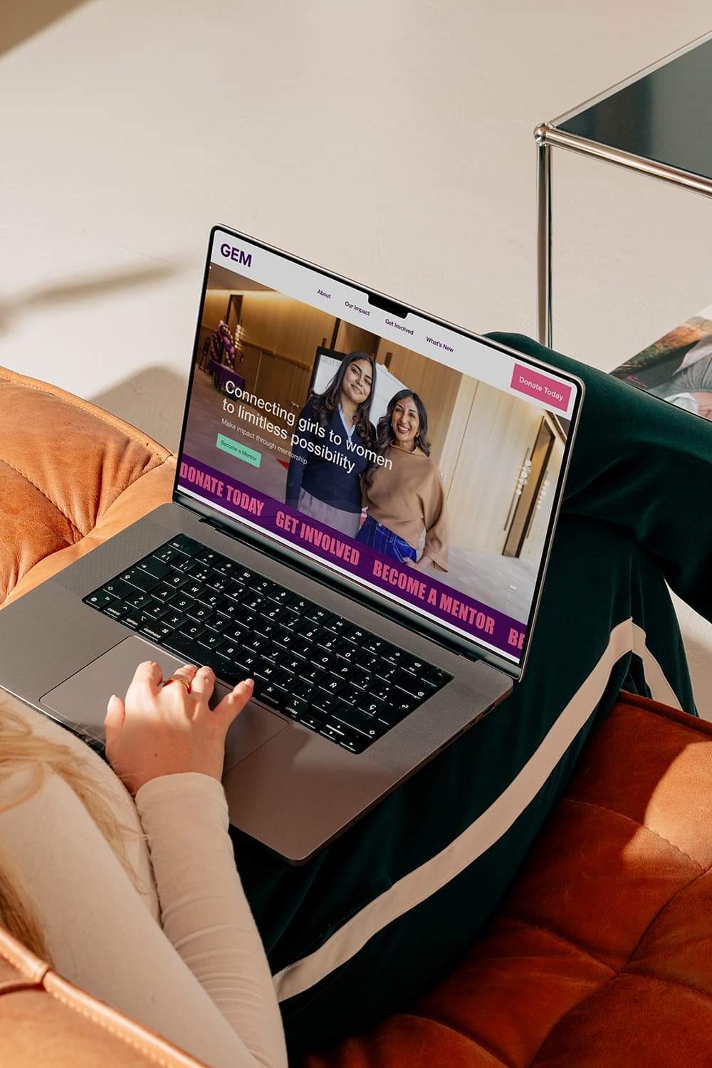 A woman holding a laptop open to a website for Girls EMentorship (GEM), designed by Sweetfolk Studio. An organization connecting girls to women