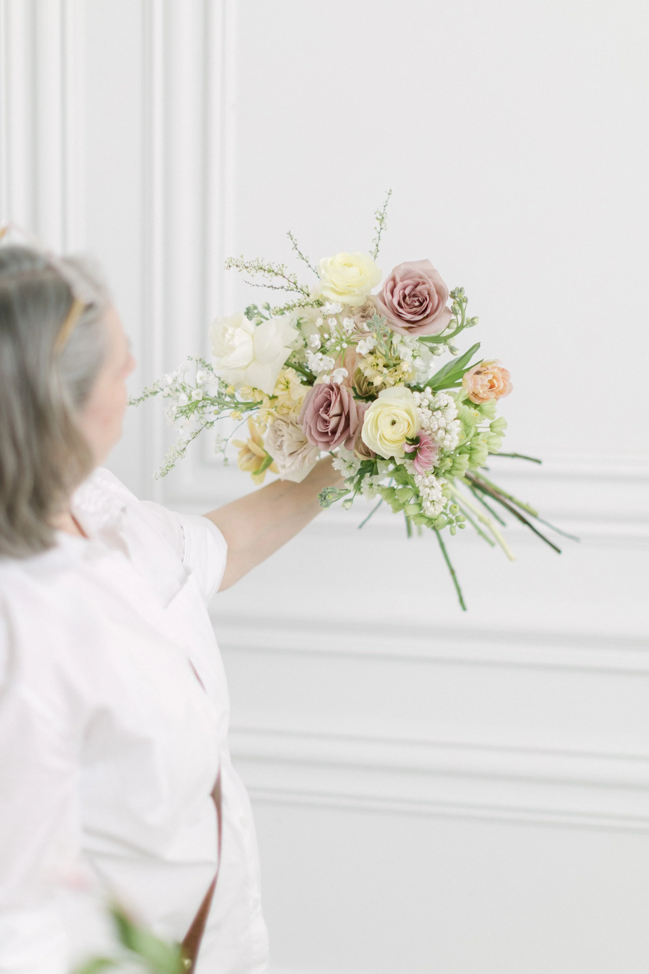 A florist from Twig & Bloom in Saskatoon is holding up some flowers in pastel colors. She is creating a beautiful bridal bouquet.
