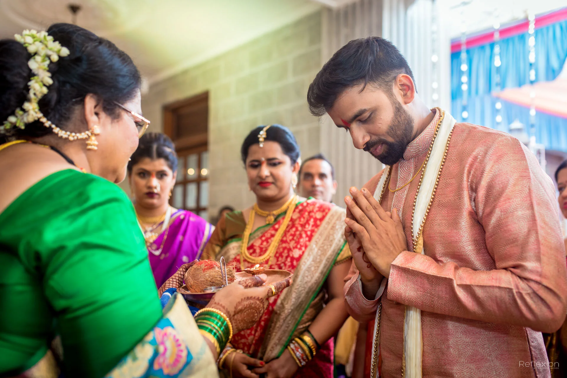 Indian wedding ceremony with a man and woman in traditional attire performing a religious ritual with family members watching.