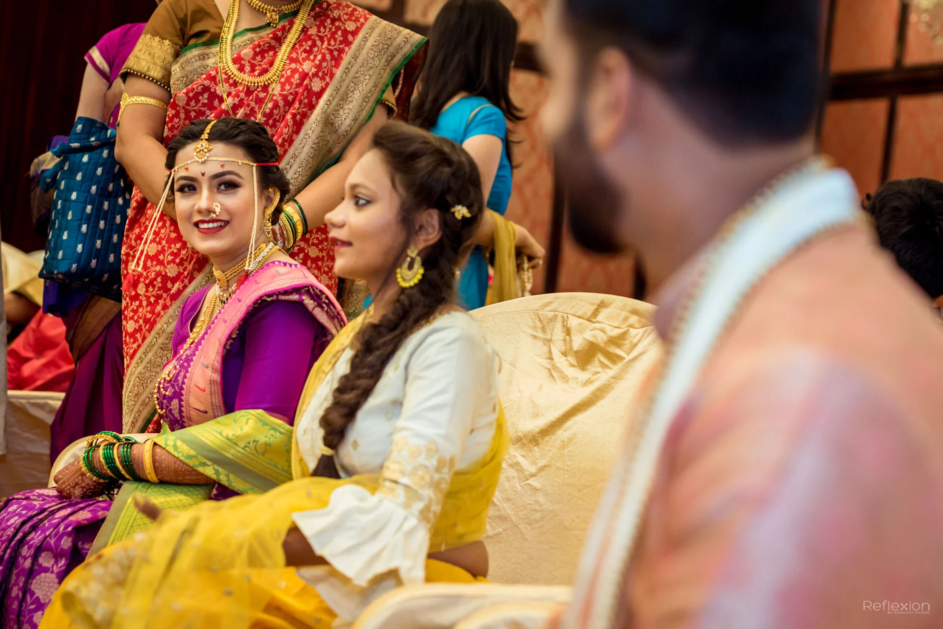 People dressed in colorful traditional Indian attire at a cultural event or ceremony, seated and engaging with each other.