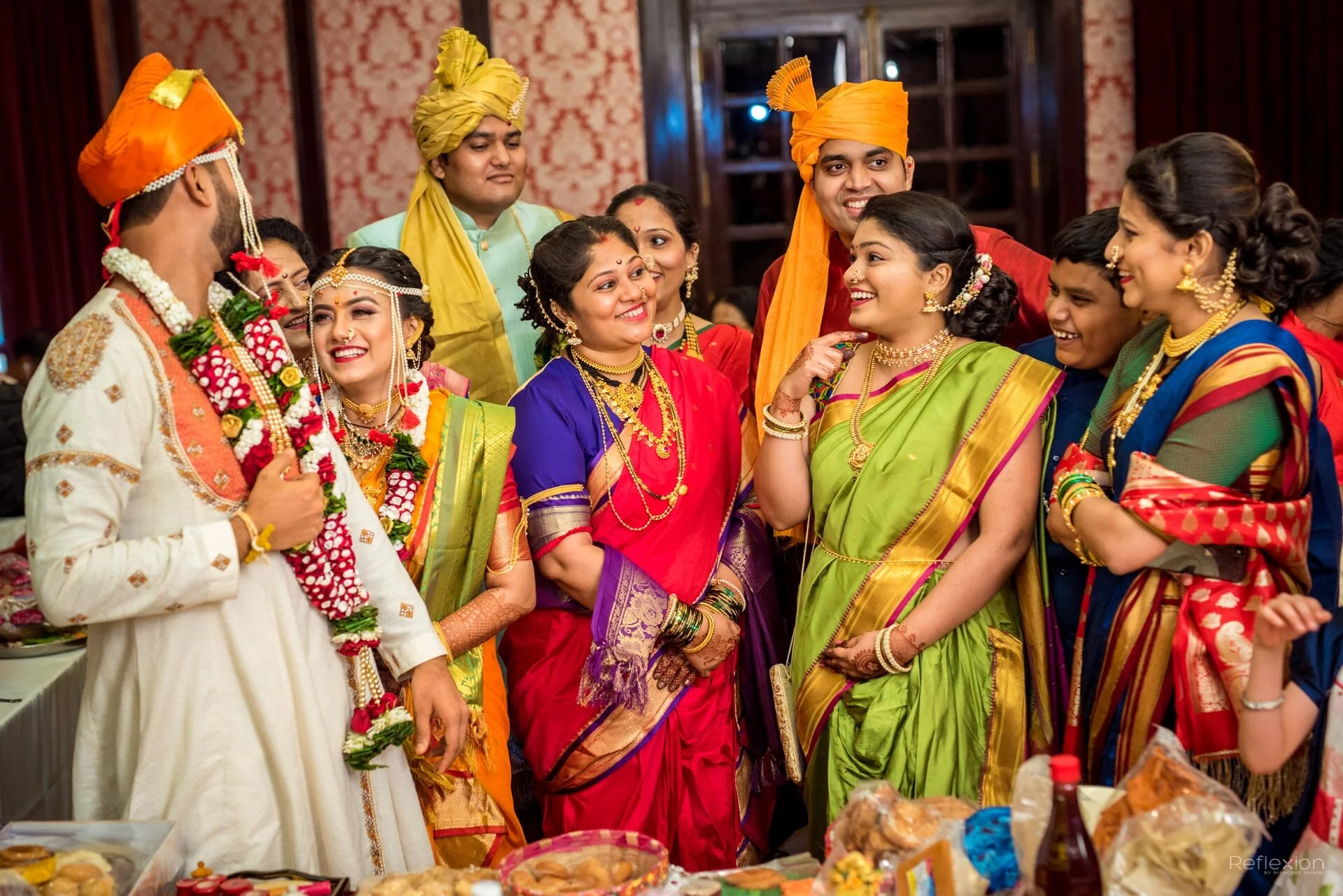 Group of people at an Indian wedding celebration, dressed in traditional colorful attire, smiling and engaging with each other.