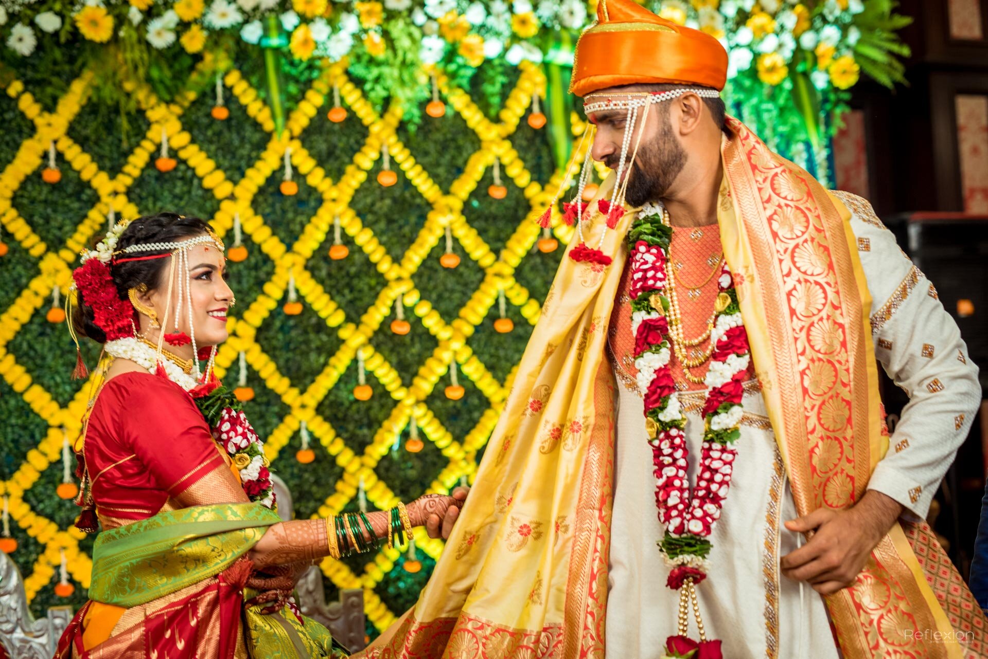 Indian bride and groom exchanging garlands during a wedding ceremony, with vibrant yellow and green floral decorations in the background.