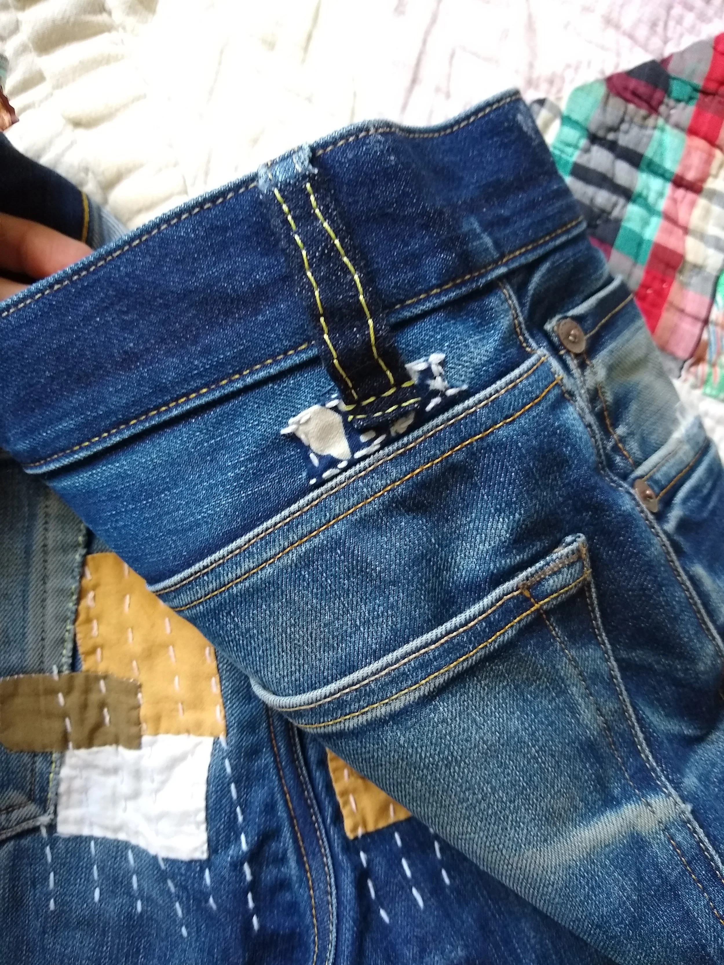 The yellow stitching and earth tone fabric patches of this mend match the yellow undertones of this denim and the contrast stitching of the original garment.