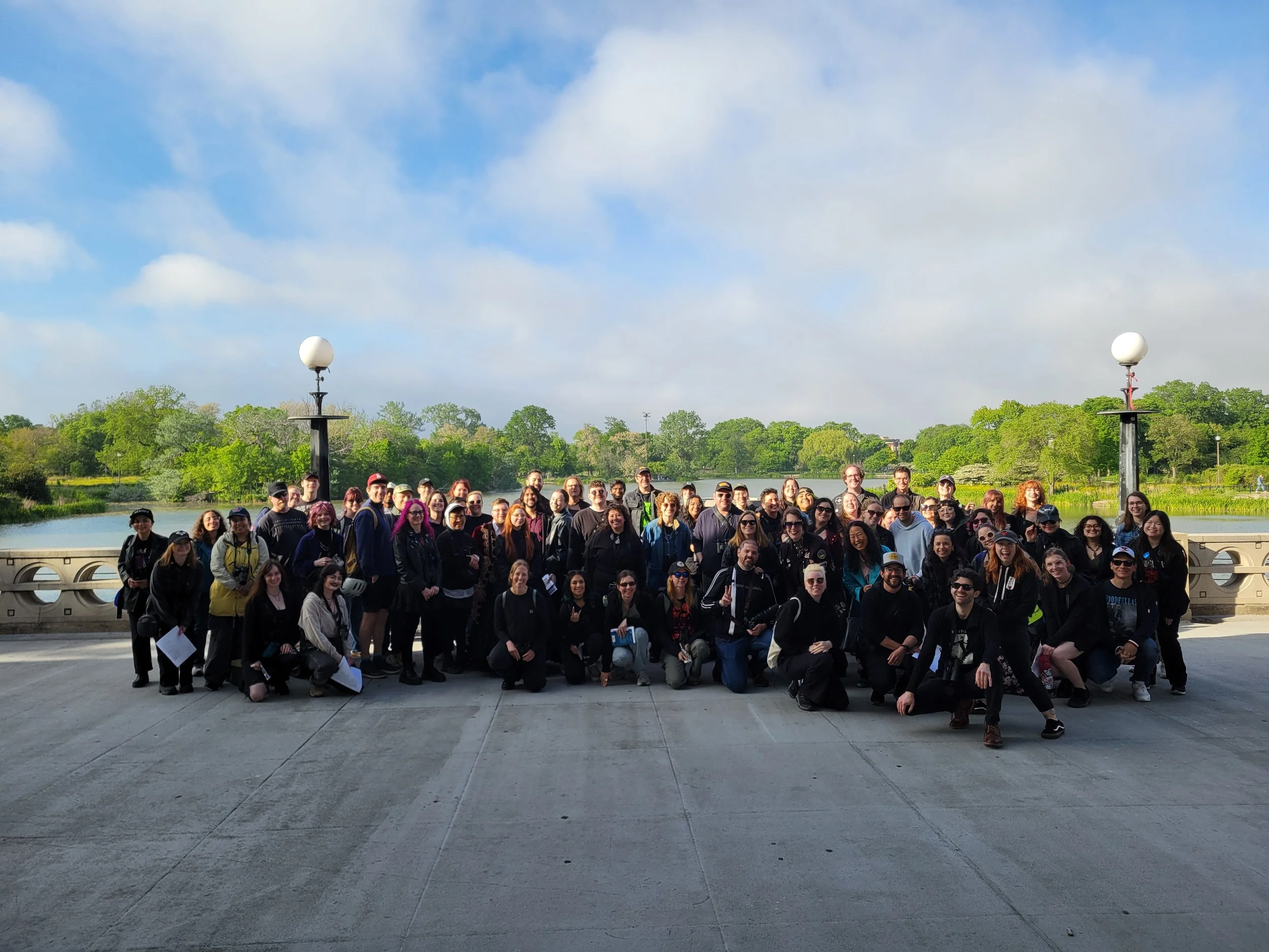 More than 50 people, nearly all in dark clothing, some standing, some kneeling, face the camera in front of the Humboldt Park lagoon.
