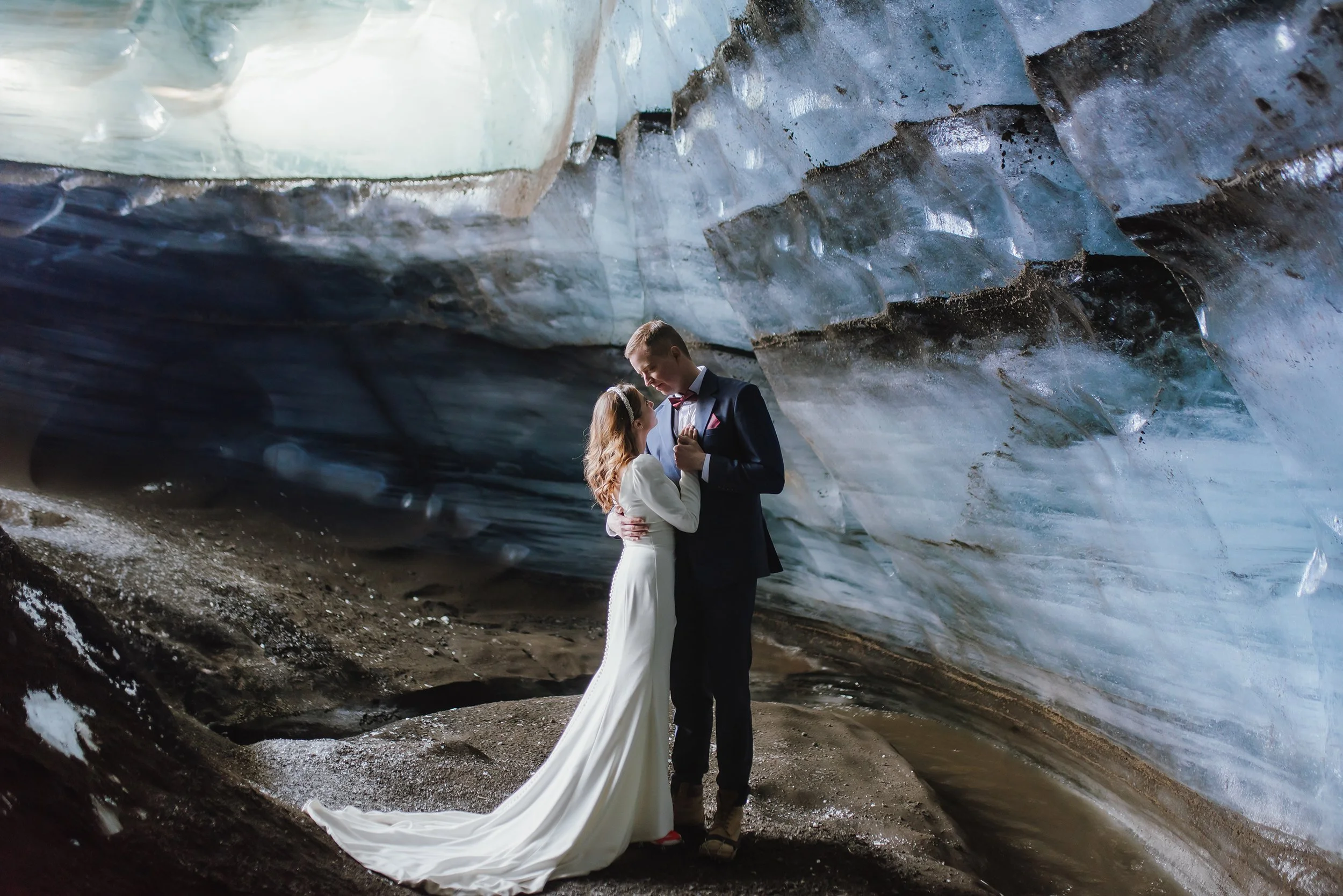 A bride and groom dancing inside a glacier cave with icy walls and a dark, rocky floor.