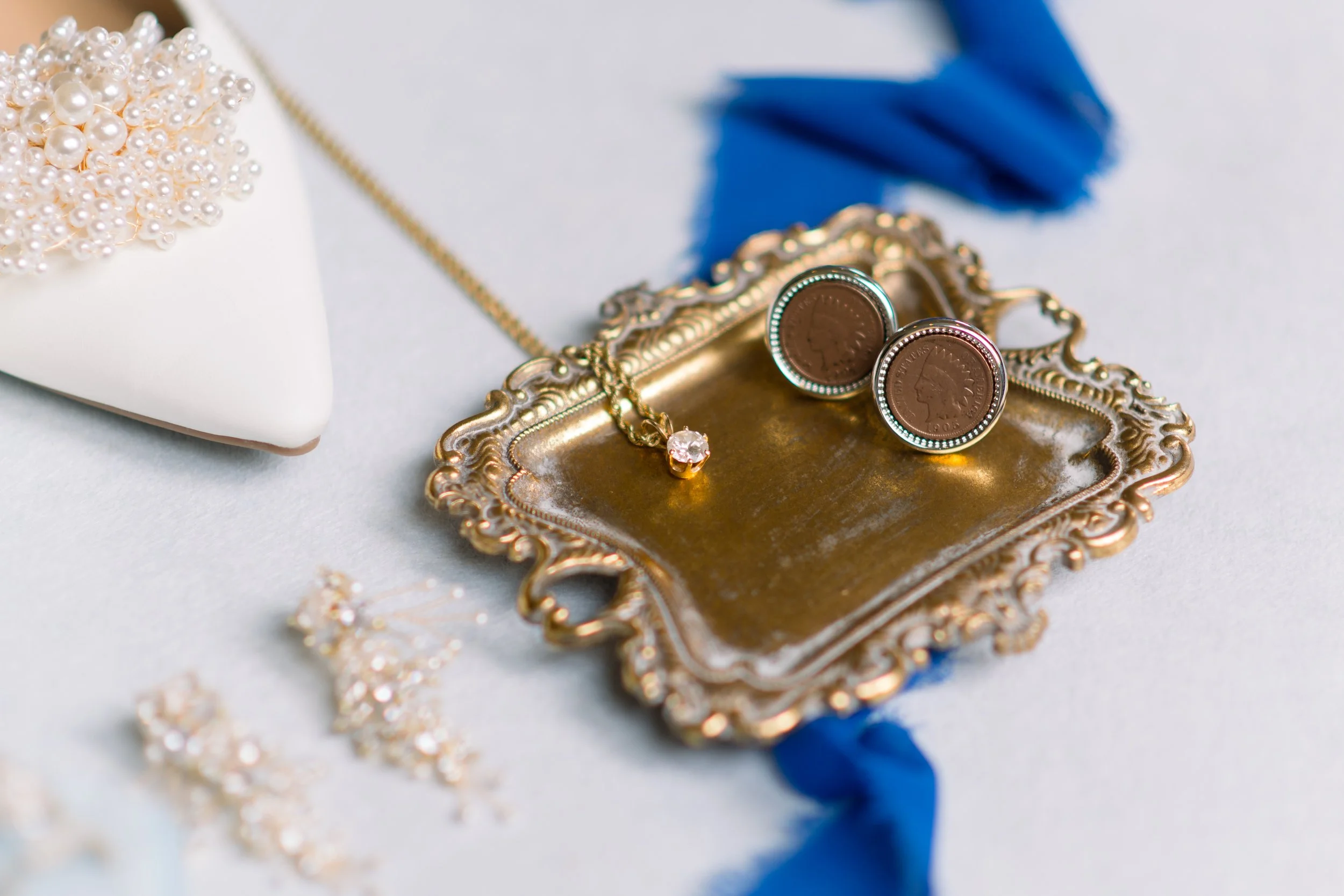 Pearl necklace and earrings on a decorative gold tray with a blue ribbon and a white jewelry box in the background.
