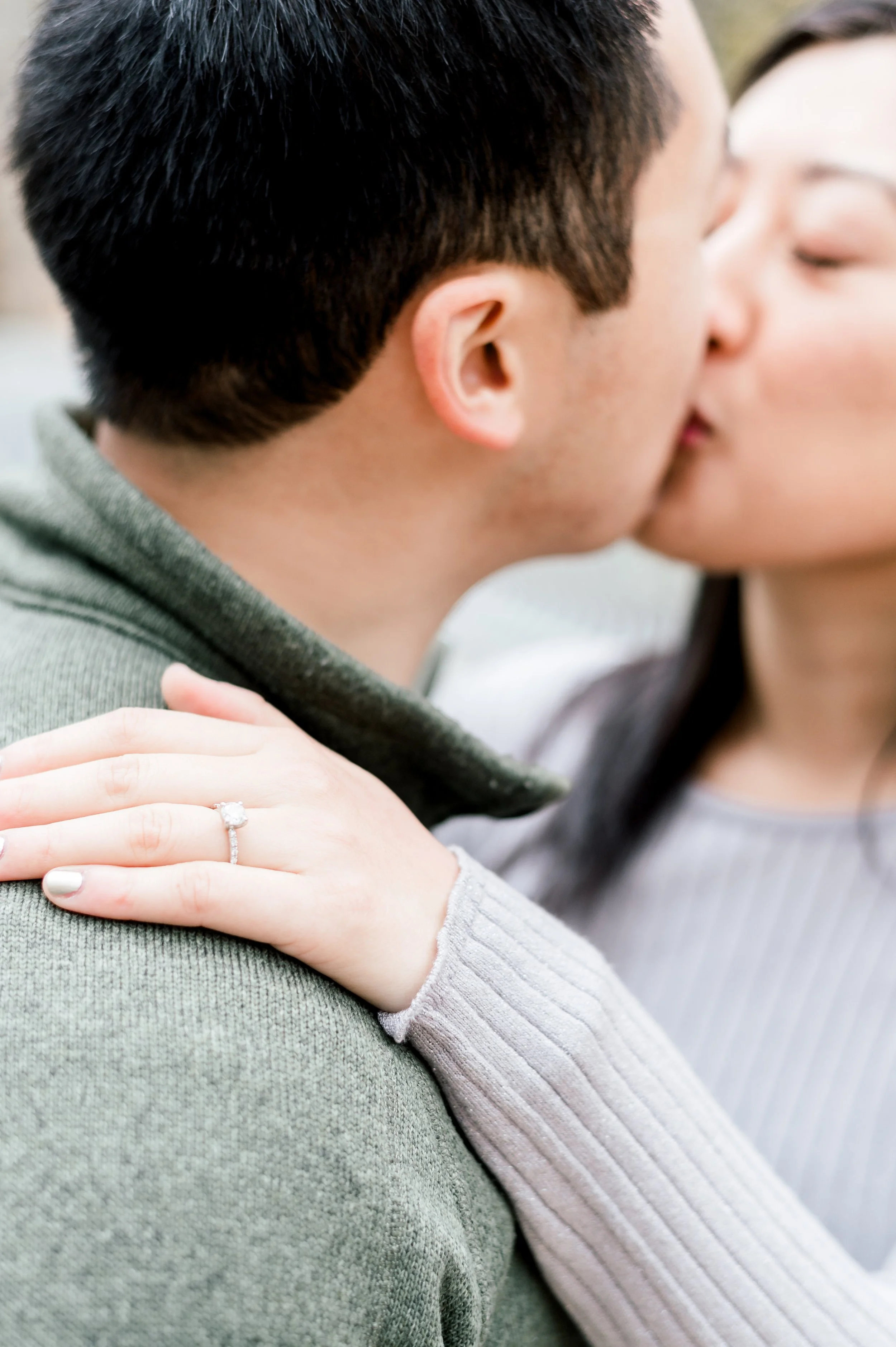 A close-up of a couple kissing, with the woman's hand resting on the man's shoulder, showcasing an engagement ring.