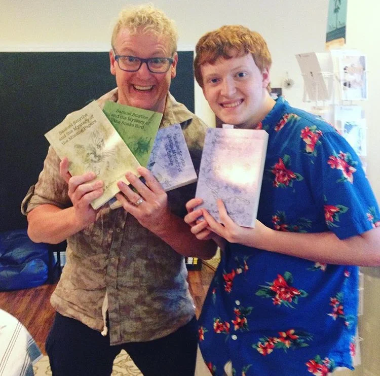 Andrew Heller, left, holds up copies of his novel trilogy with his son and inspiration for the series, Sam, right.
