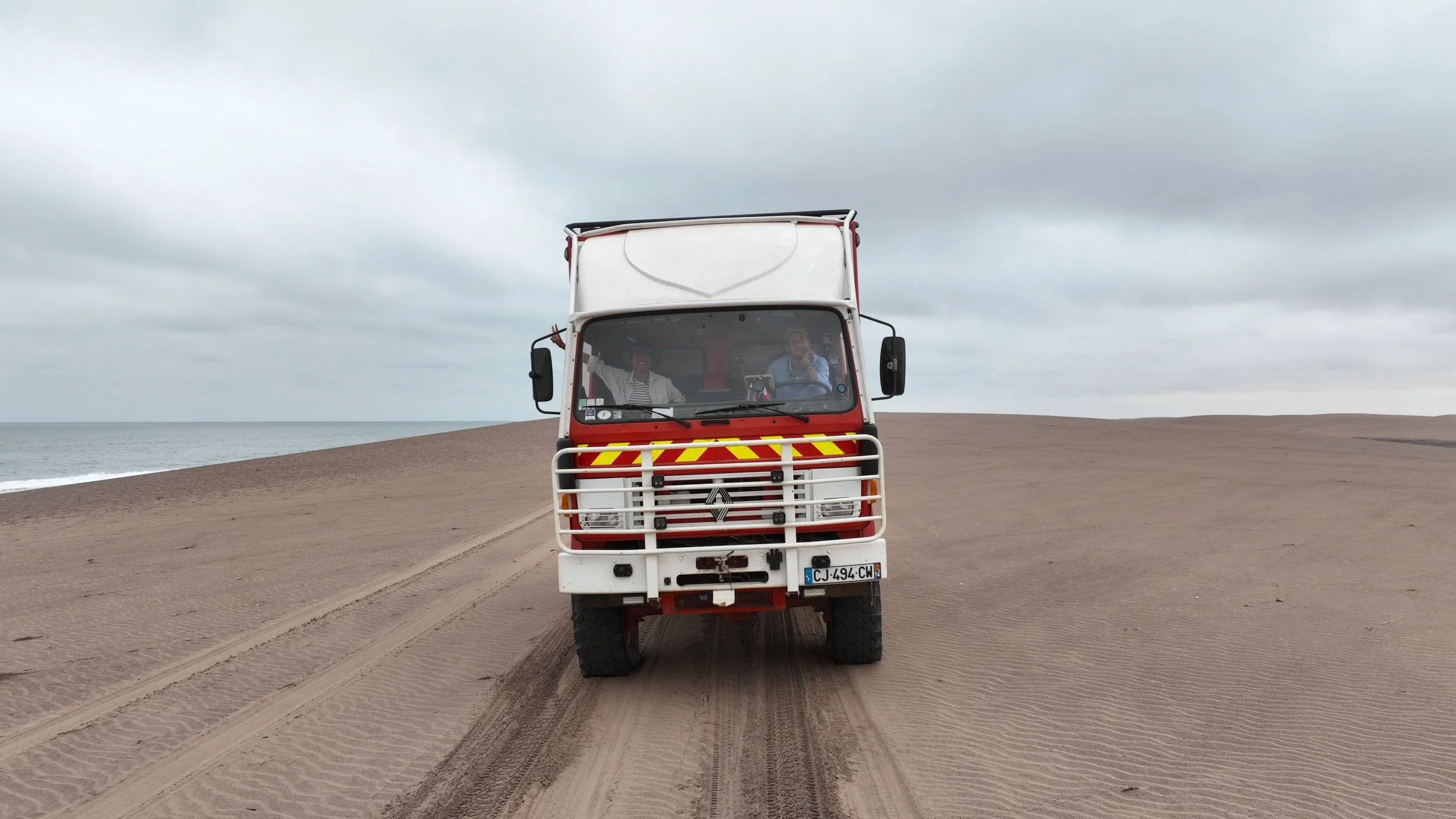Justin et Bee dans le RedTruck, conduisant sur une plage de sable en Angola lors de leur traversée de l’Afrique en camion d’expédition.